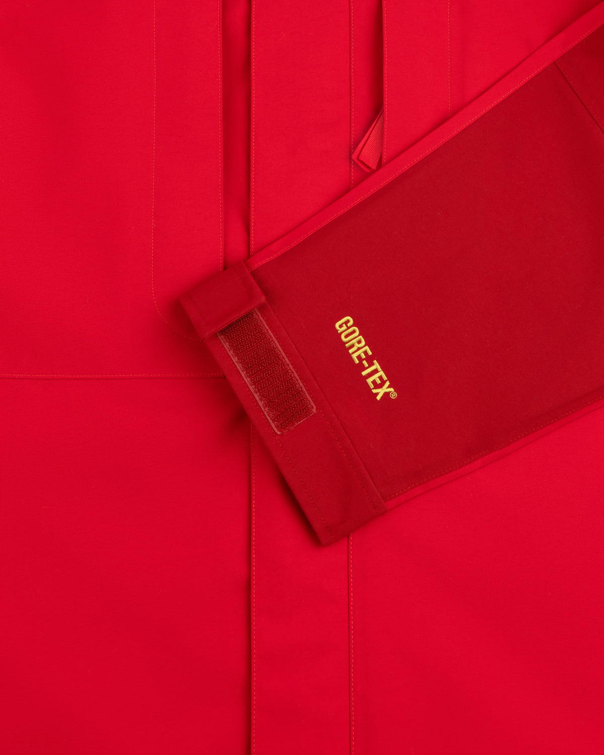 Close-up of ALD / The North Face GORE-TEX 2000 Mountain Jacket sleeve with yellow logo, Velcro strap, red background.