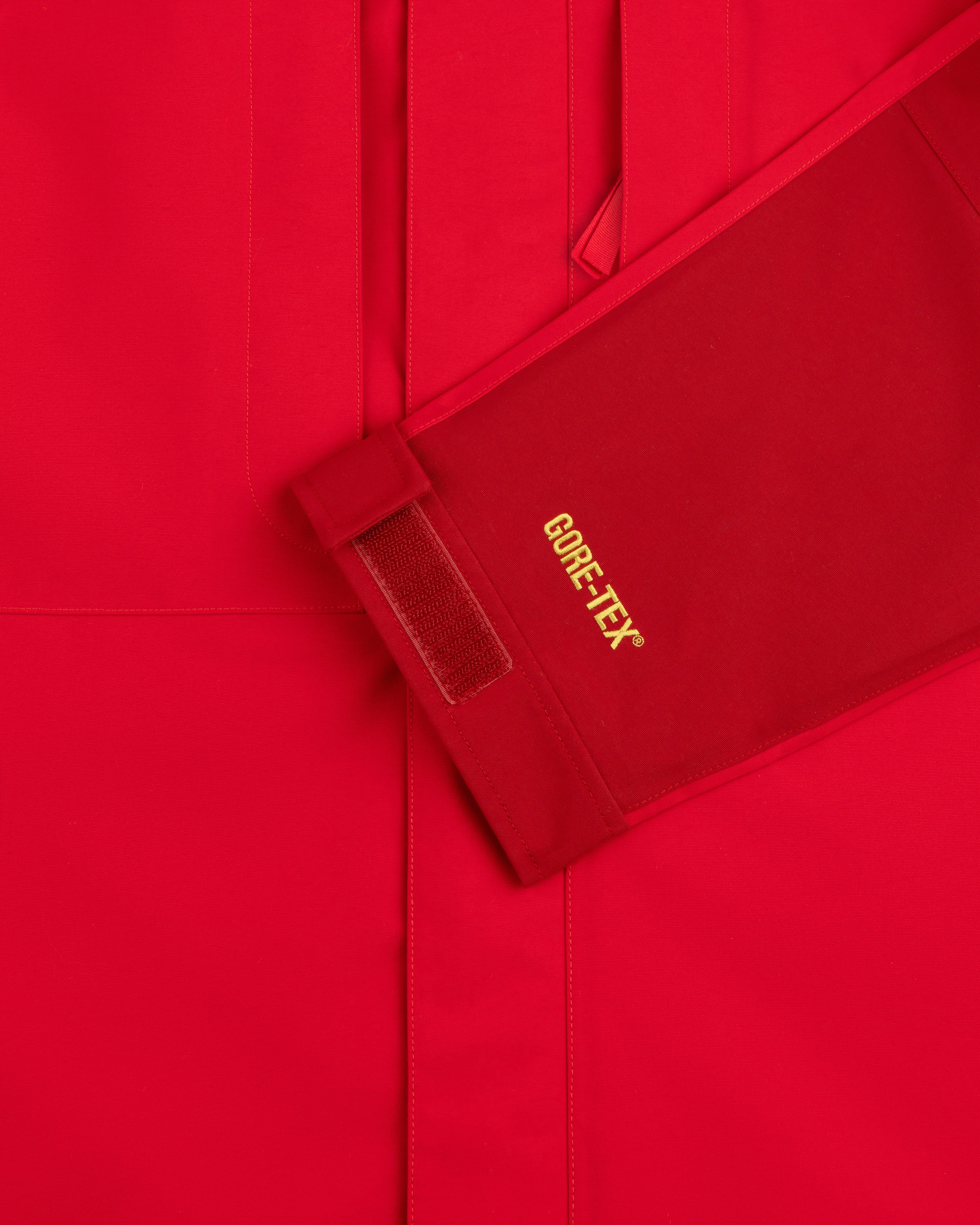 Close-up of ALD / The North Face GORE-TEX 2000 Mountain Jacket sleeve with yellow logo, Velcro strap, red background.