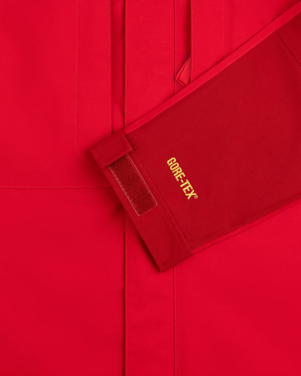 Close-up of ALD / The North Face GORE-TEX 2000 Mountain Jacket sleeve with yellow logo, Velcro strap, red background.