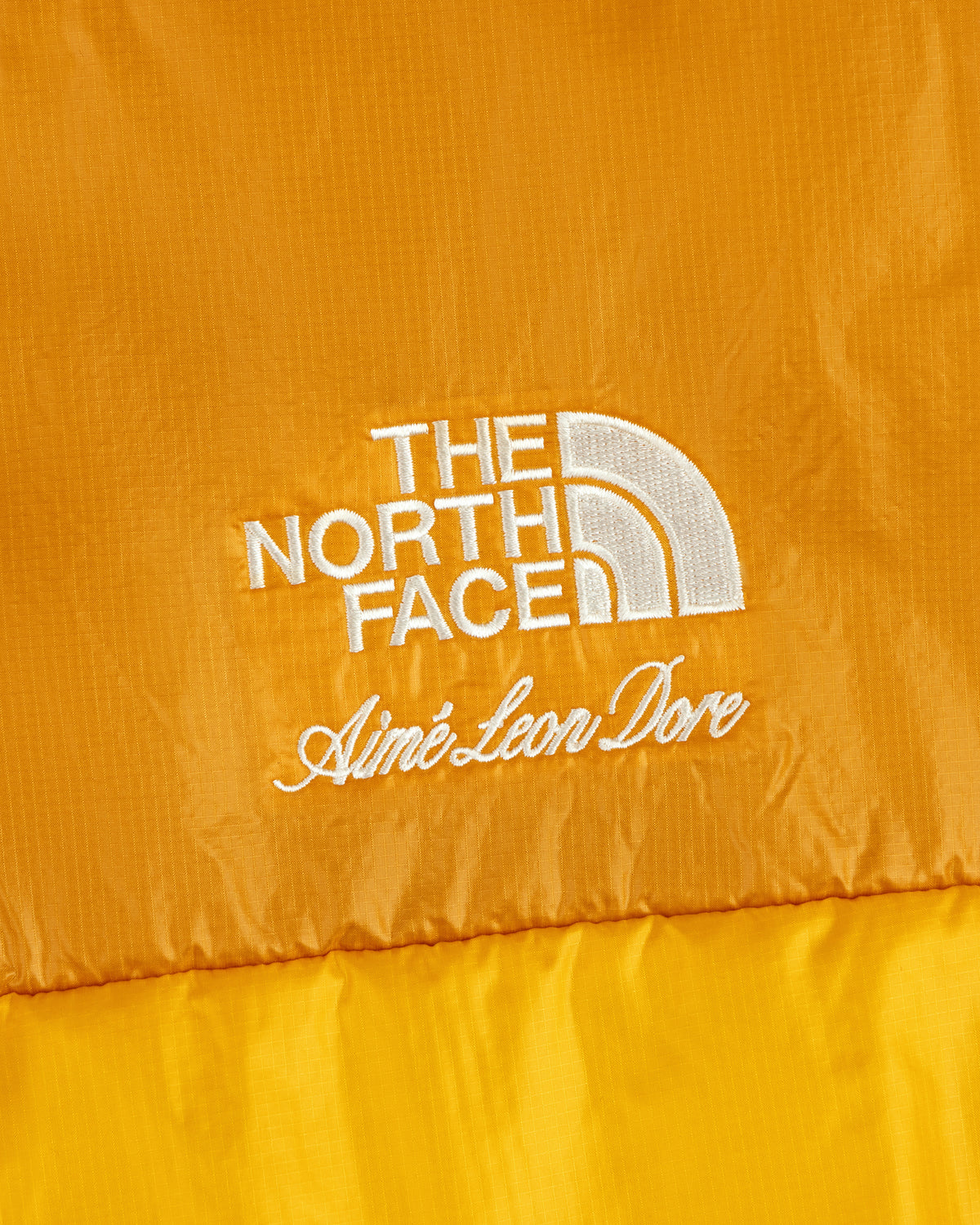 Close-up of yellow ALD / The North Face Reversible Pertex® Nuptse Jacket, white embroidery visible.