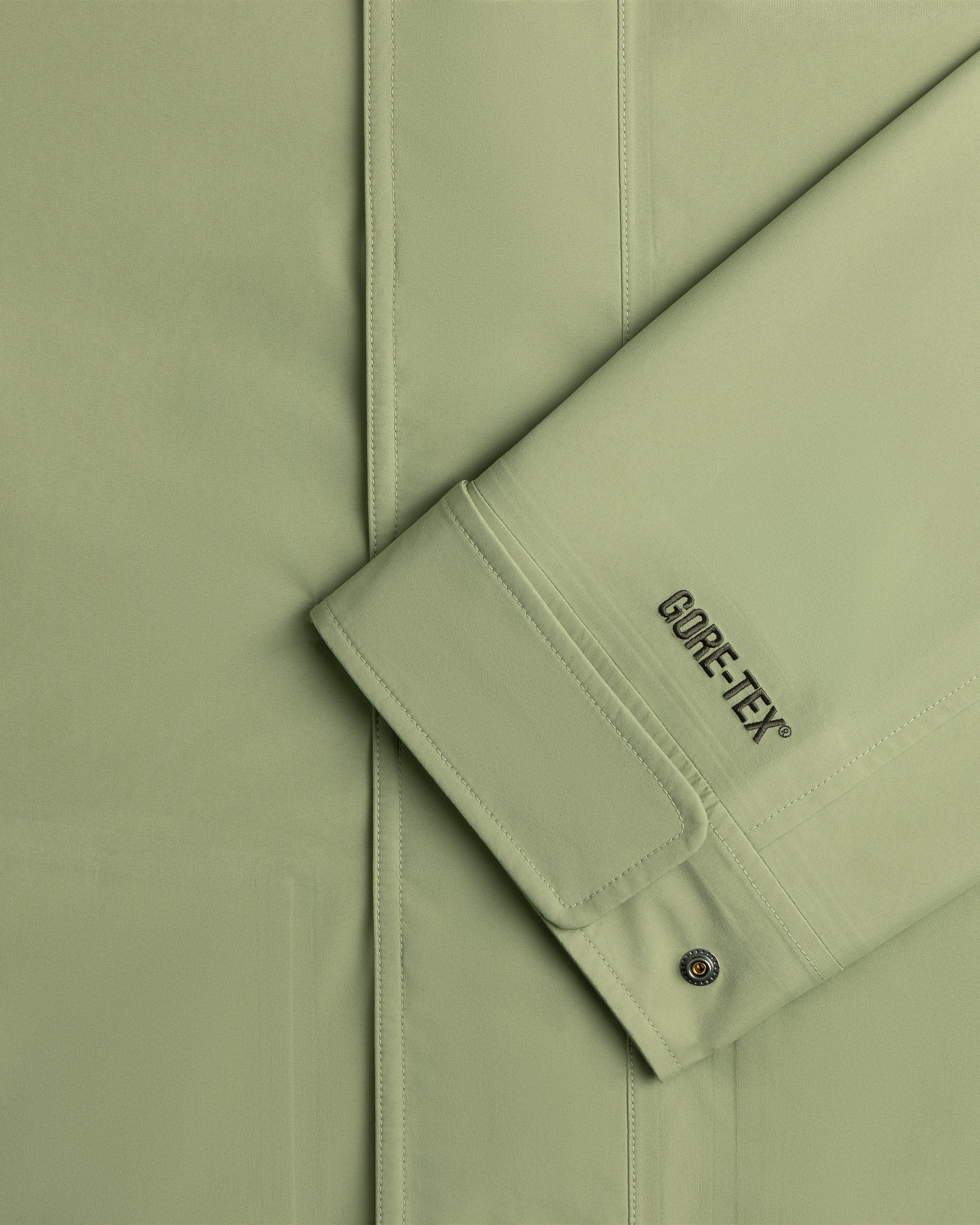 Close-up of ALD / The North Face GORE-TEX Trench Coat sleeve with branding and a metal snap button on the cuff.