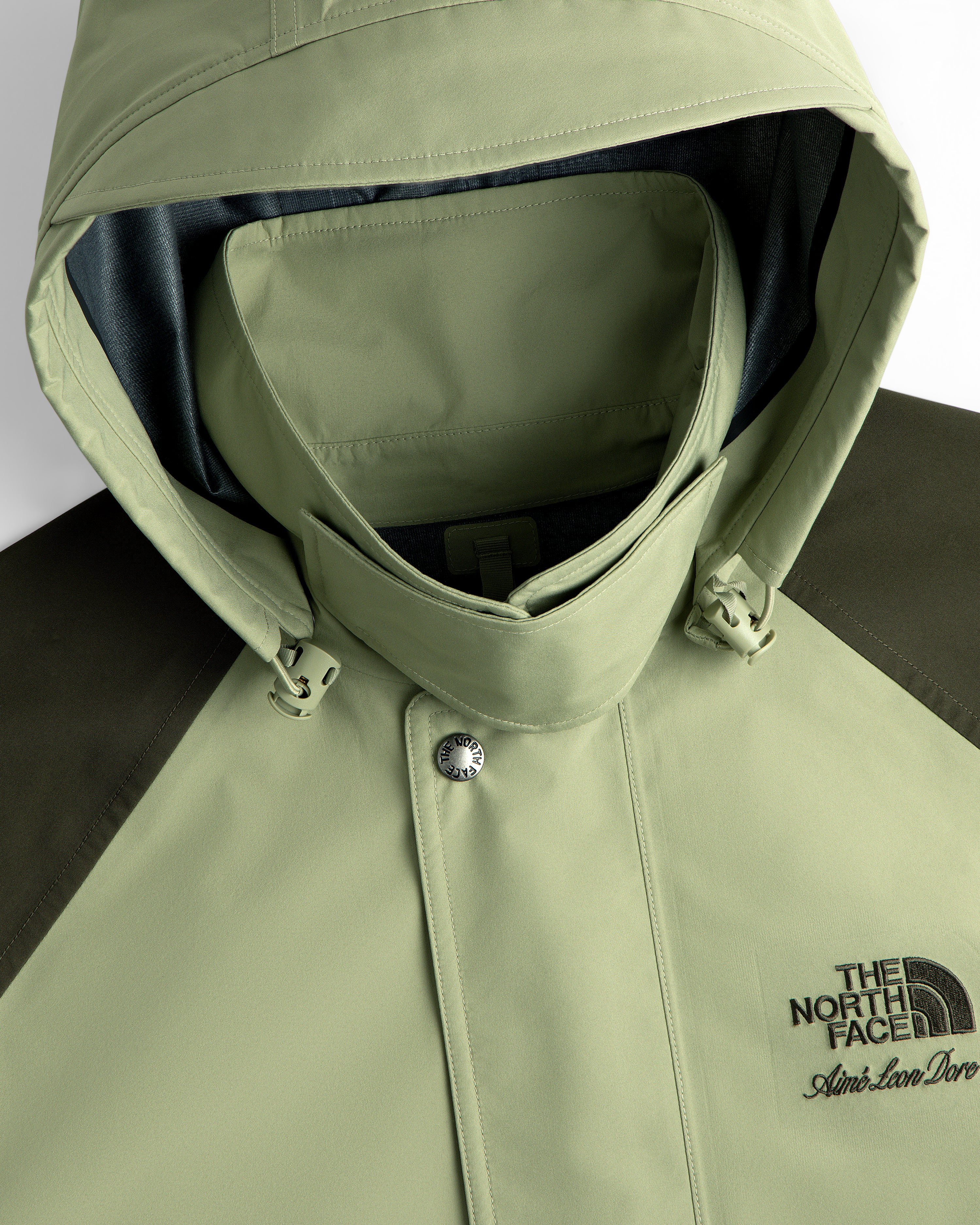 Light green ALD / The North Face GORE-TEX Trench Coat with chest logos, shown in close-up.