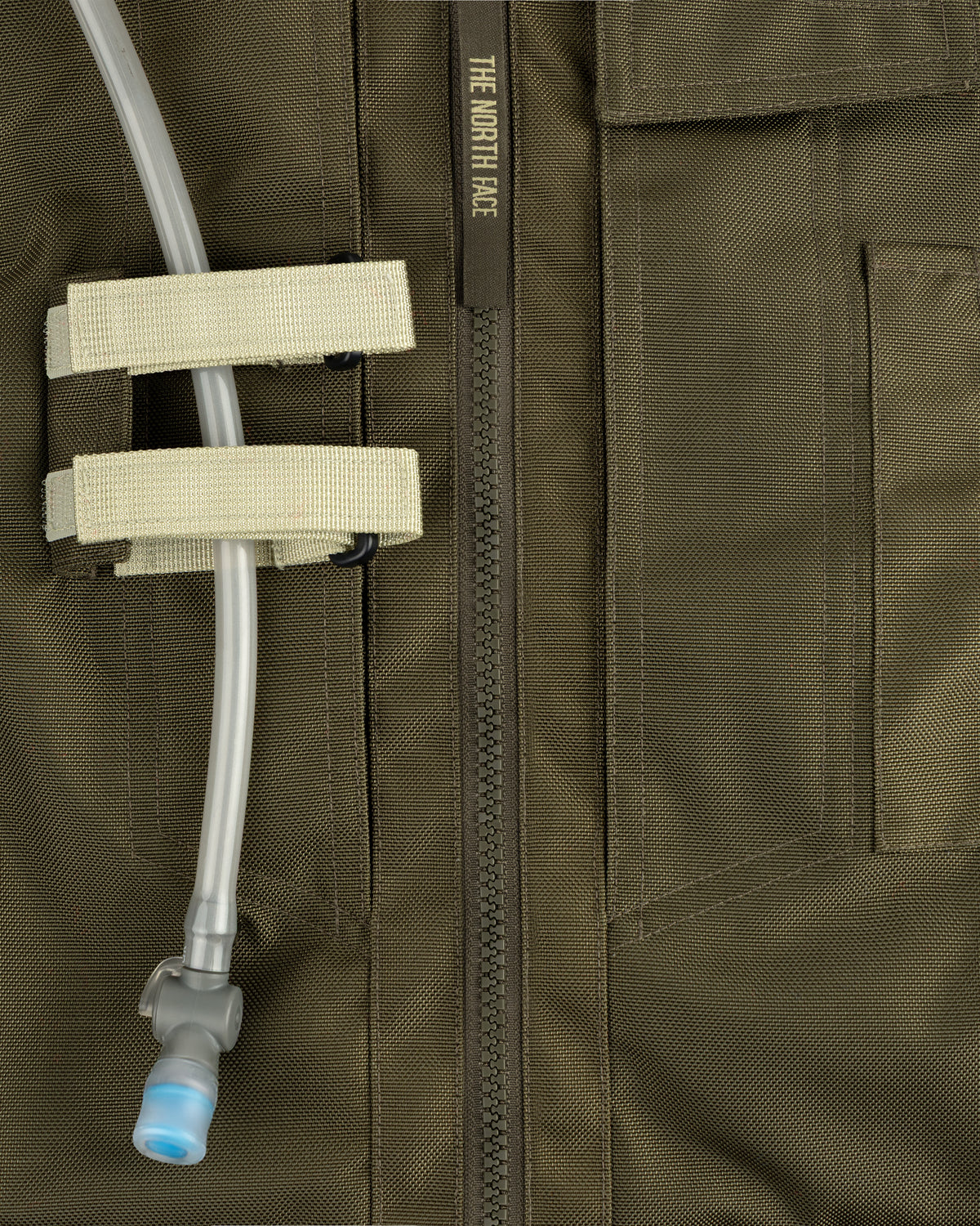 Close-up of an olive green ALD / The North Face Ballistic Tech Vest with a hydration tube in beige straps.
