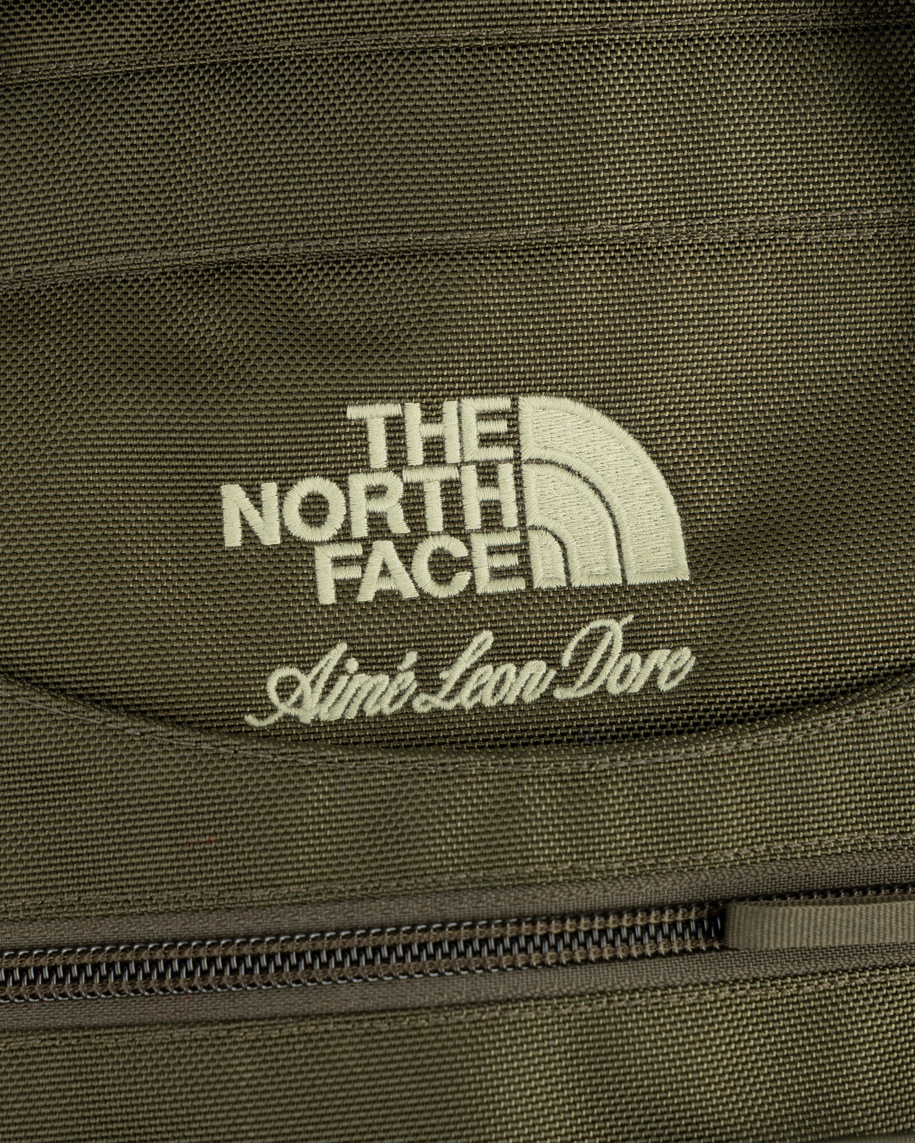 Close-up of olive green ALD / The North Face Ballistic Tech Vest with both brands’ logos above a zipper.