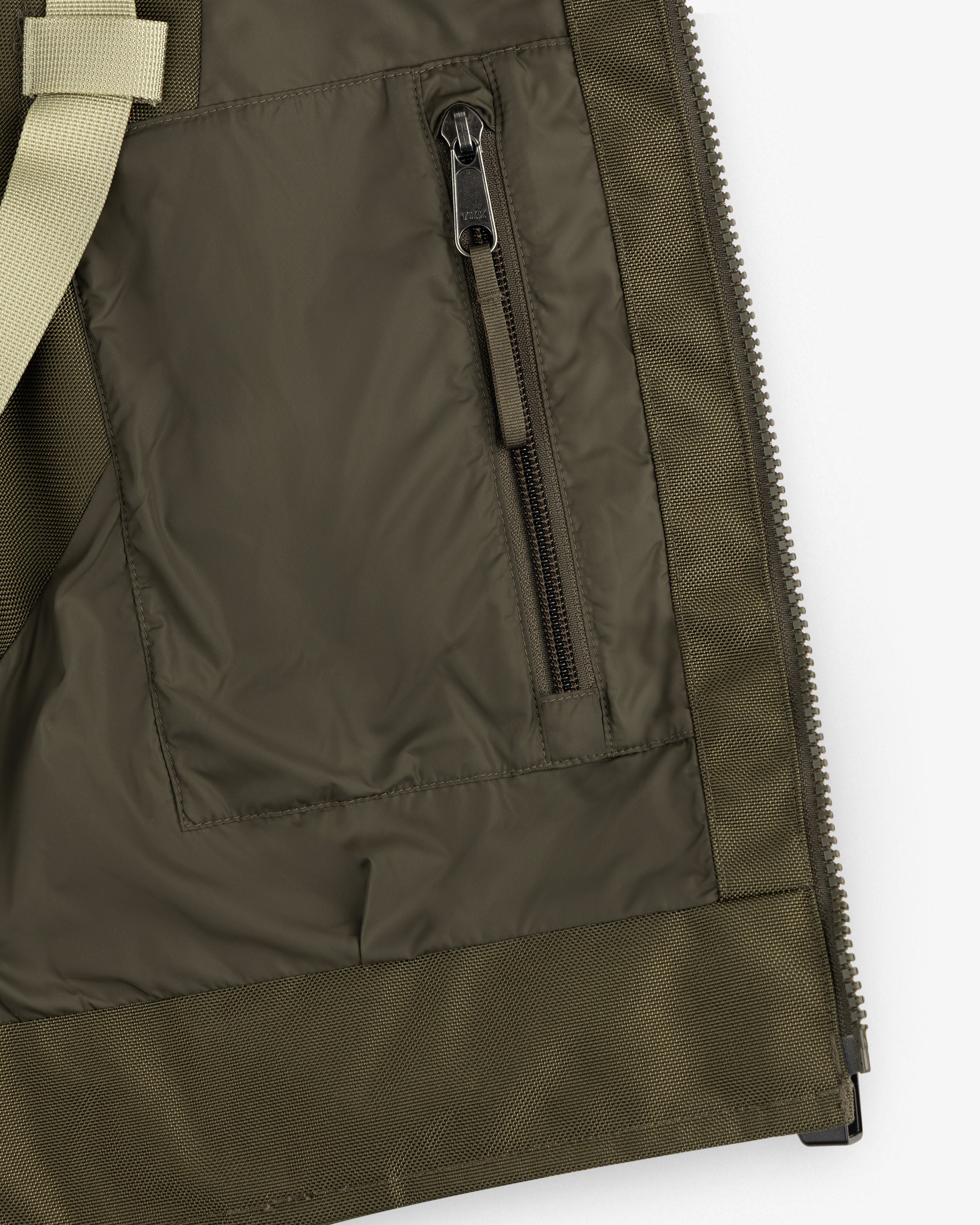 Close-up of the ALD / The North Face Ballistic Tech Vest pocket with vertical zipper and beige strap on the left.