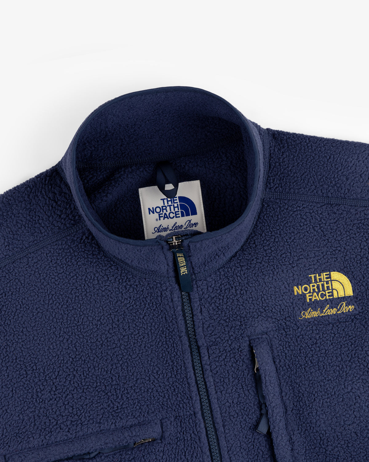 Close-up of a navy ALD / The North Face ’95 Denali Half-Zip Fleece Pullover with yellow logo and chest pocket.
