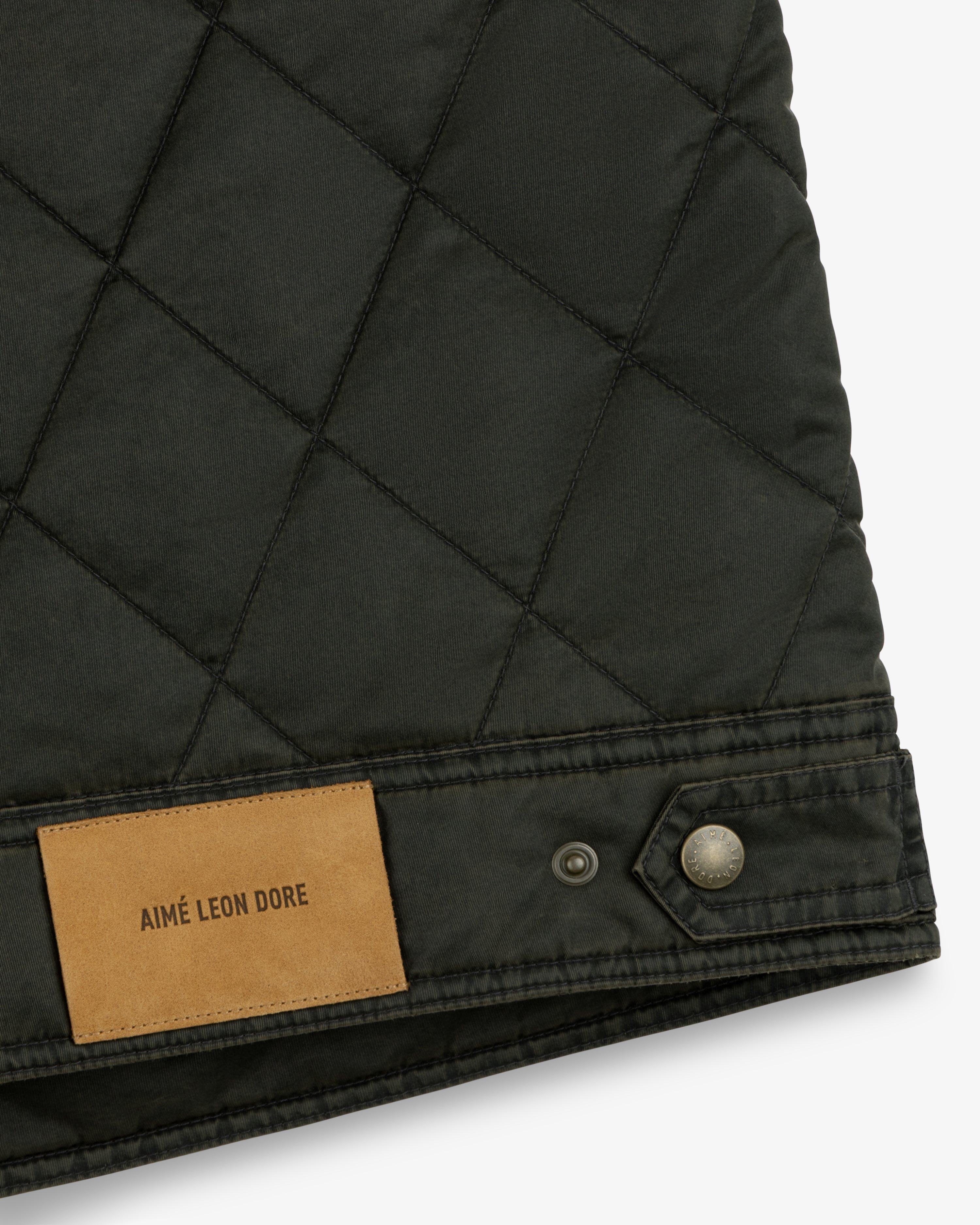 Dark green Quilted Trucker Jacket with a tan leather brand patch and a metal button on the hem.