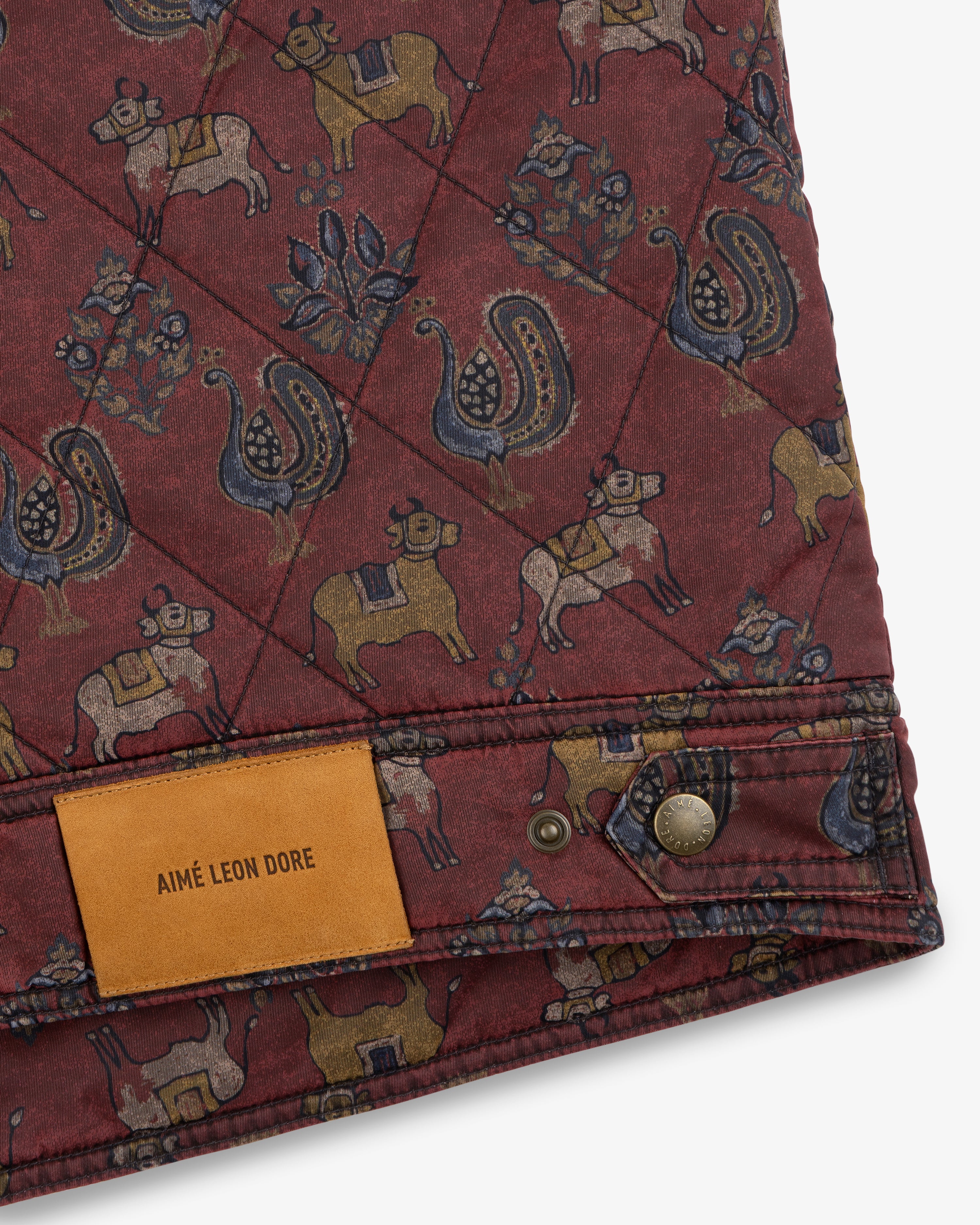 Quilted Trucker Jacket in maroon with a cow and peacock pattern, featuring a tan leather label and metal button.