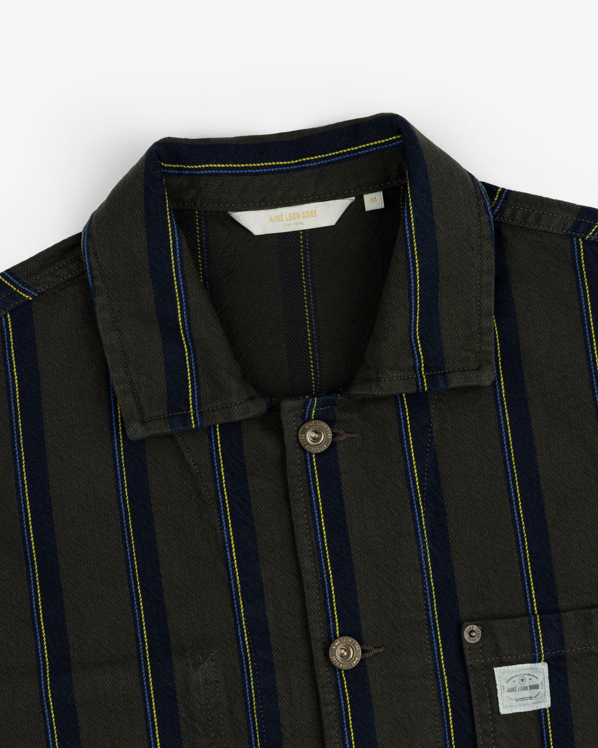 Close-up of a Striped Denim Chore Jacket with a collar and visible fabric label on the chest pocket.