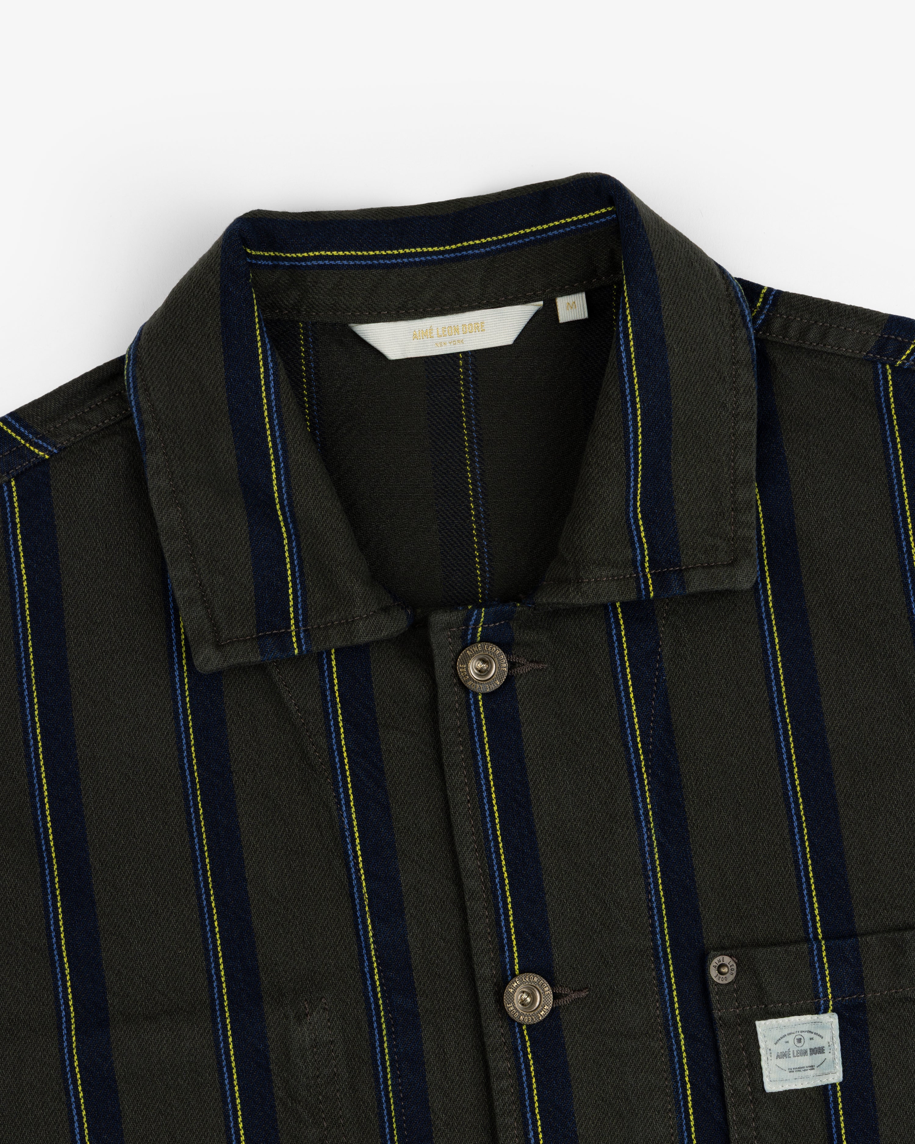 Close-up of a Striped Denim Chore Jacket with a collar and visible fabric label on the chest pocket.