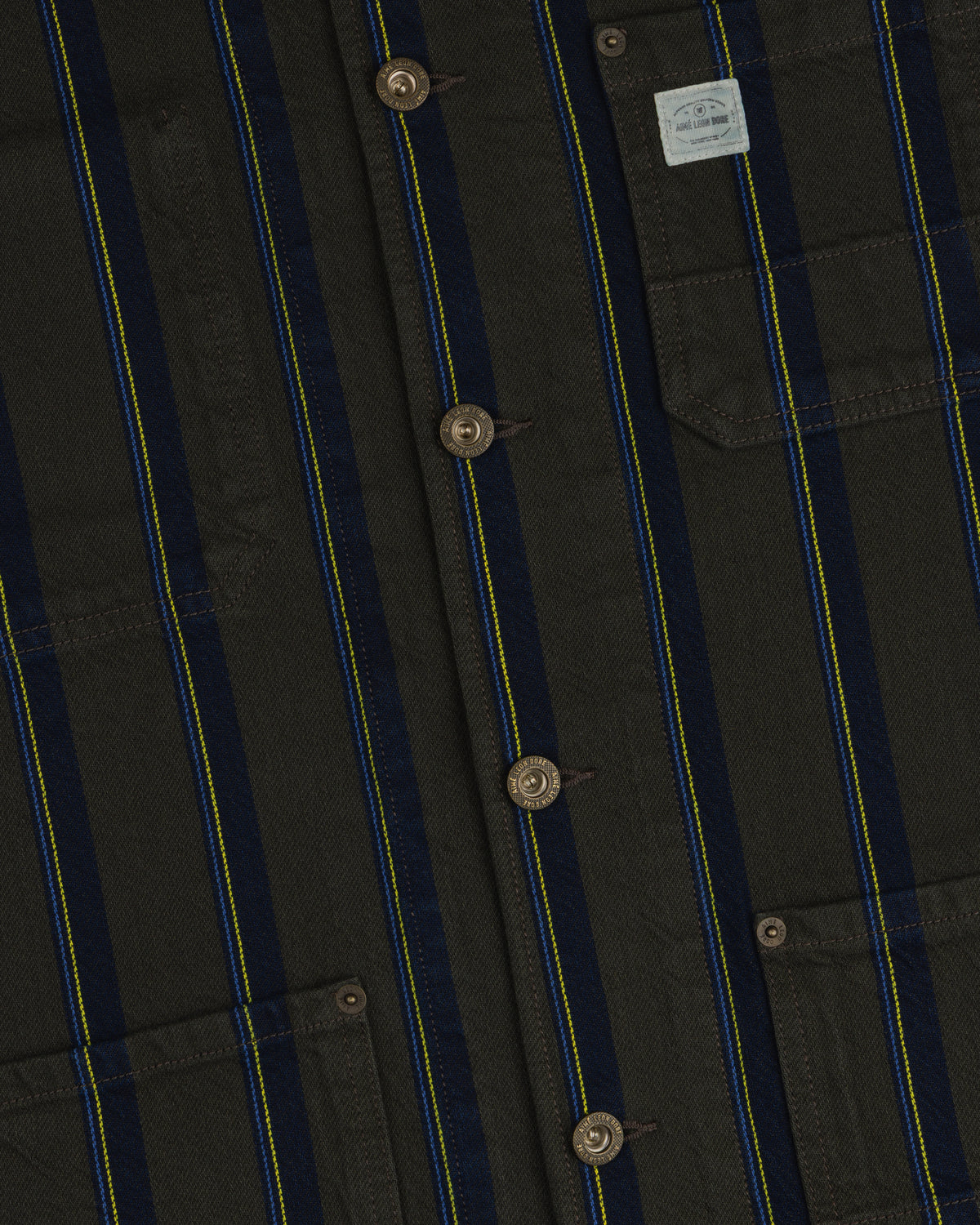 Close-up of the Striped Denim Chore Jacket with blue/yellow stripes, brown buttons, and a pocket label.