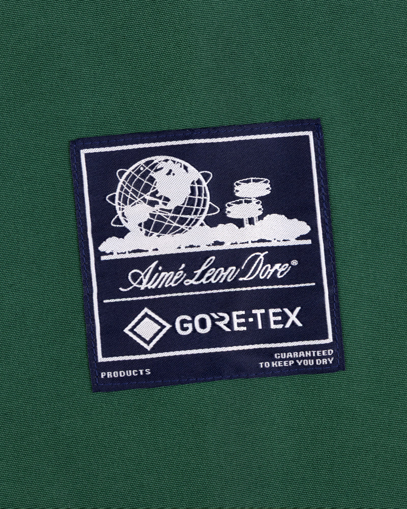 A navy GORE-TEX Striped Sailing Jacket patch on green, with a globe, clouds, and text by Aimé Leon Dore.