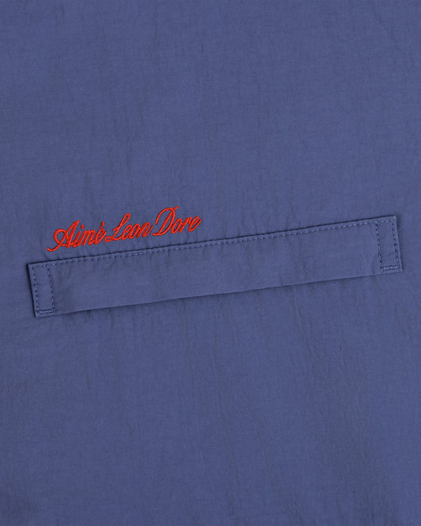 Blue fleece lined windbreaker with a horizontal stitched flap and red cursive Aimé Leon Dore above the flap.