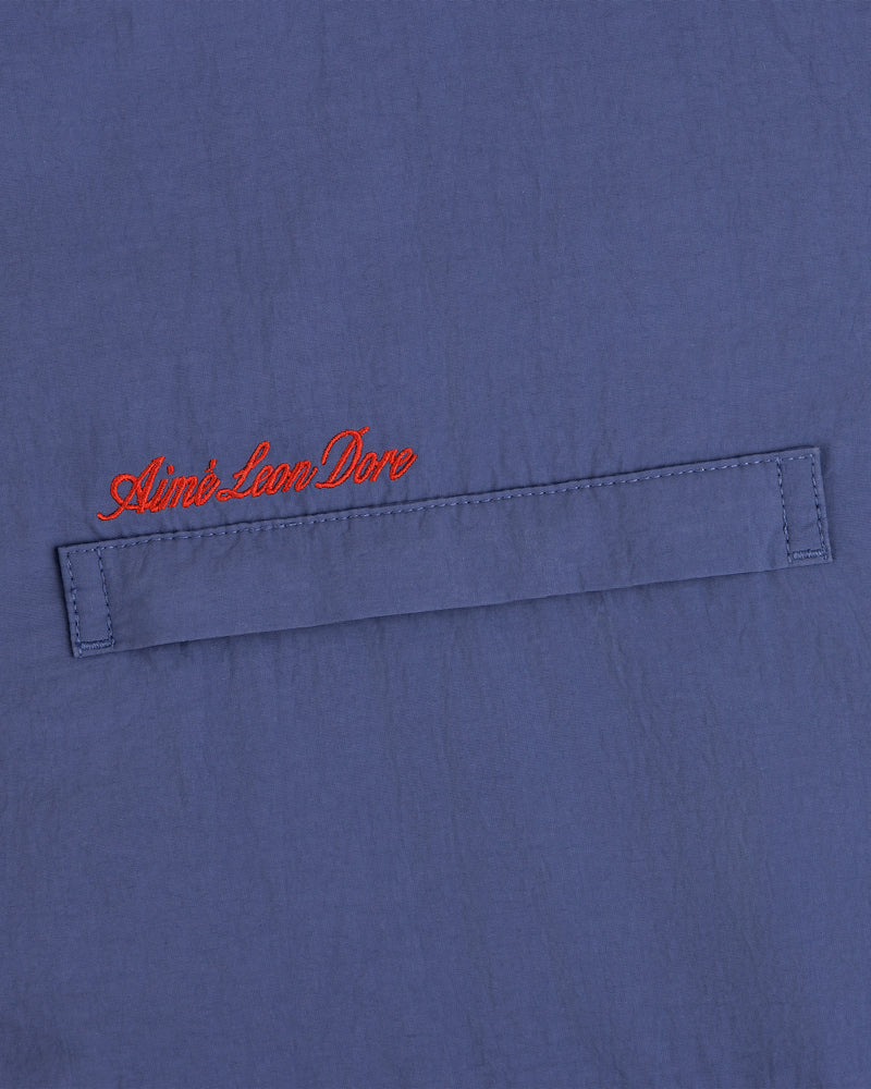 Blue fleece lined windbreaker with a horizontal stitched flap and red cursive Aimé Leon Dore above the flap.