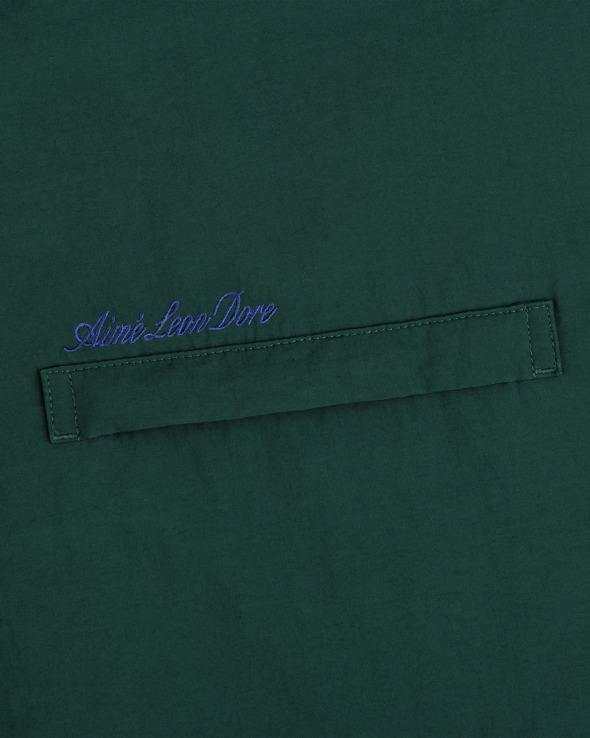 Green fleece lined sport windbreaker with blue Aimé Leon Dore cursive above a stitched horizontal fabric tab.