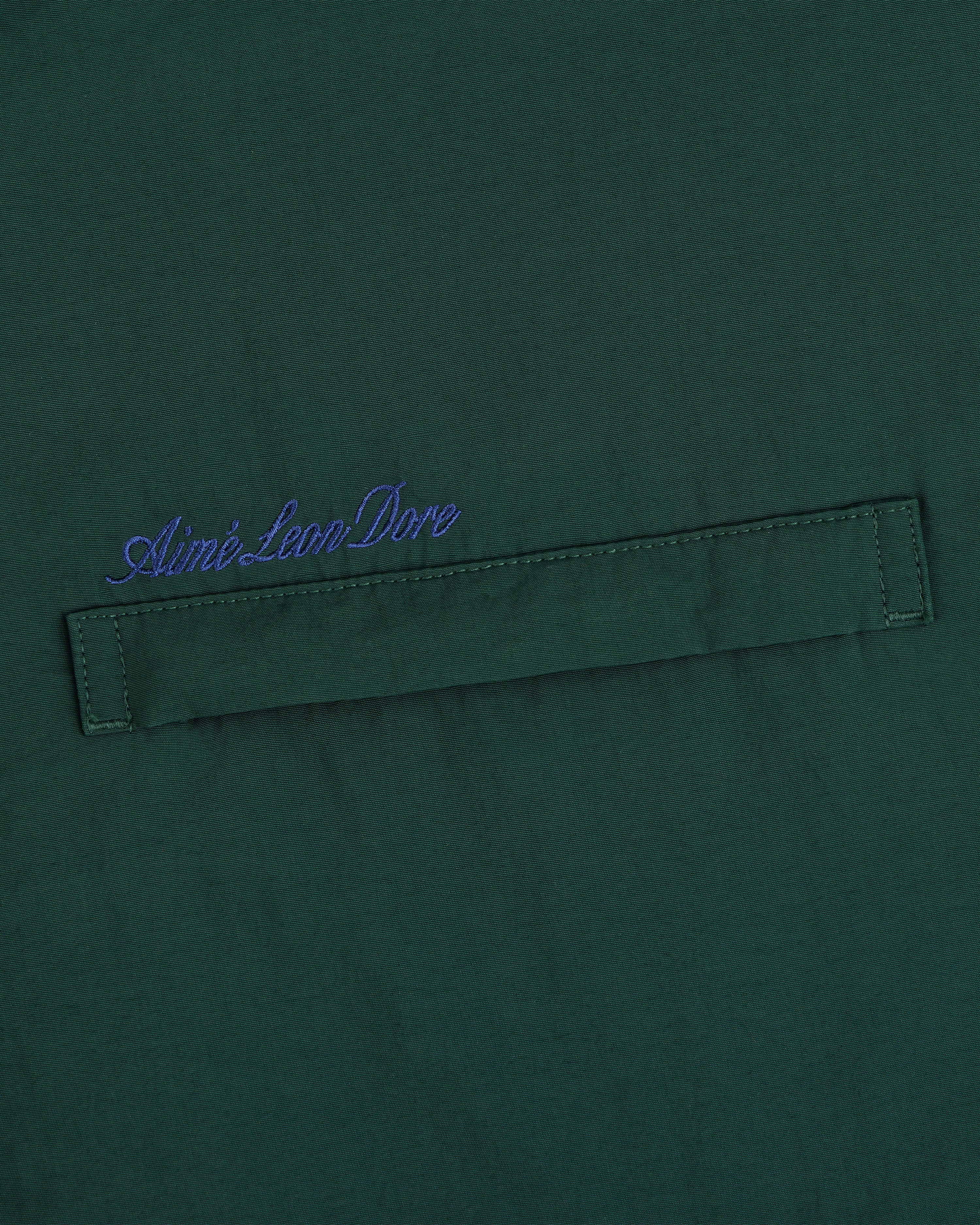 Green fleece lined sport windbreaker with blue Aimé Leon Dore cursive above a stitched horizontal fabric tab.