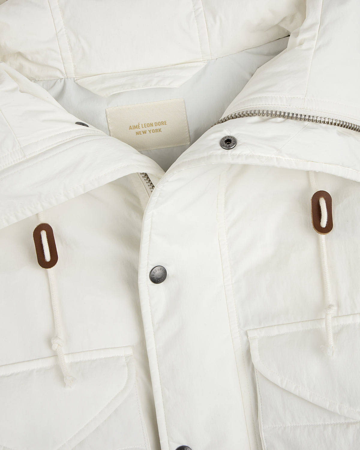 Close-up of a white Down-Filled Surplus Parka with a zipper, button placket, two front pockets, and brown drawstring toggles.