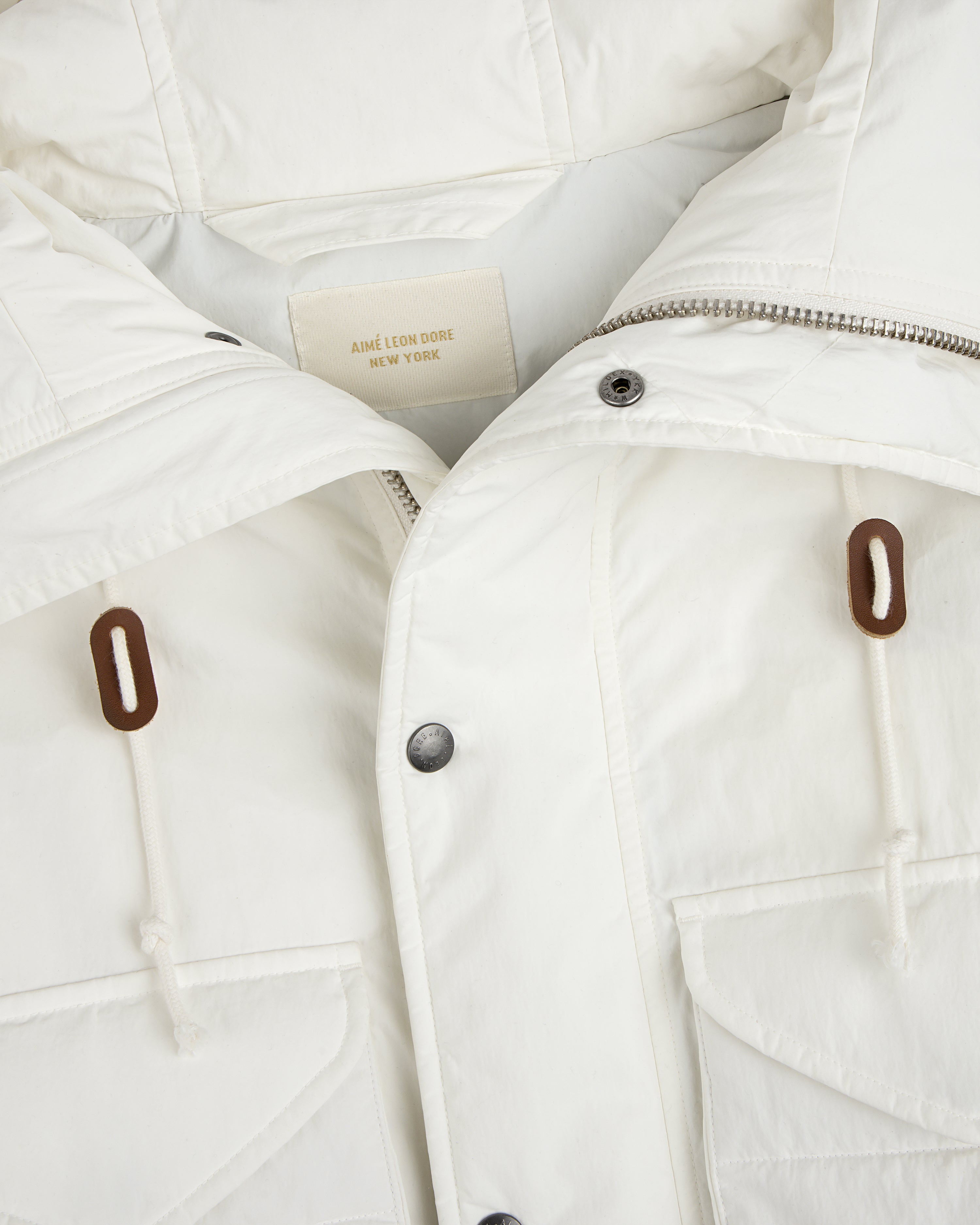 Close-up of a white Down-Filled Surplus Parka with a zipper, button placket, two front pockets, and brown drawstring toggles.