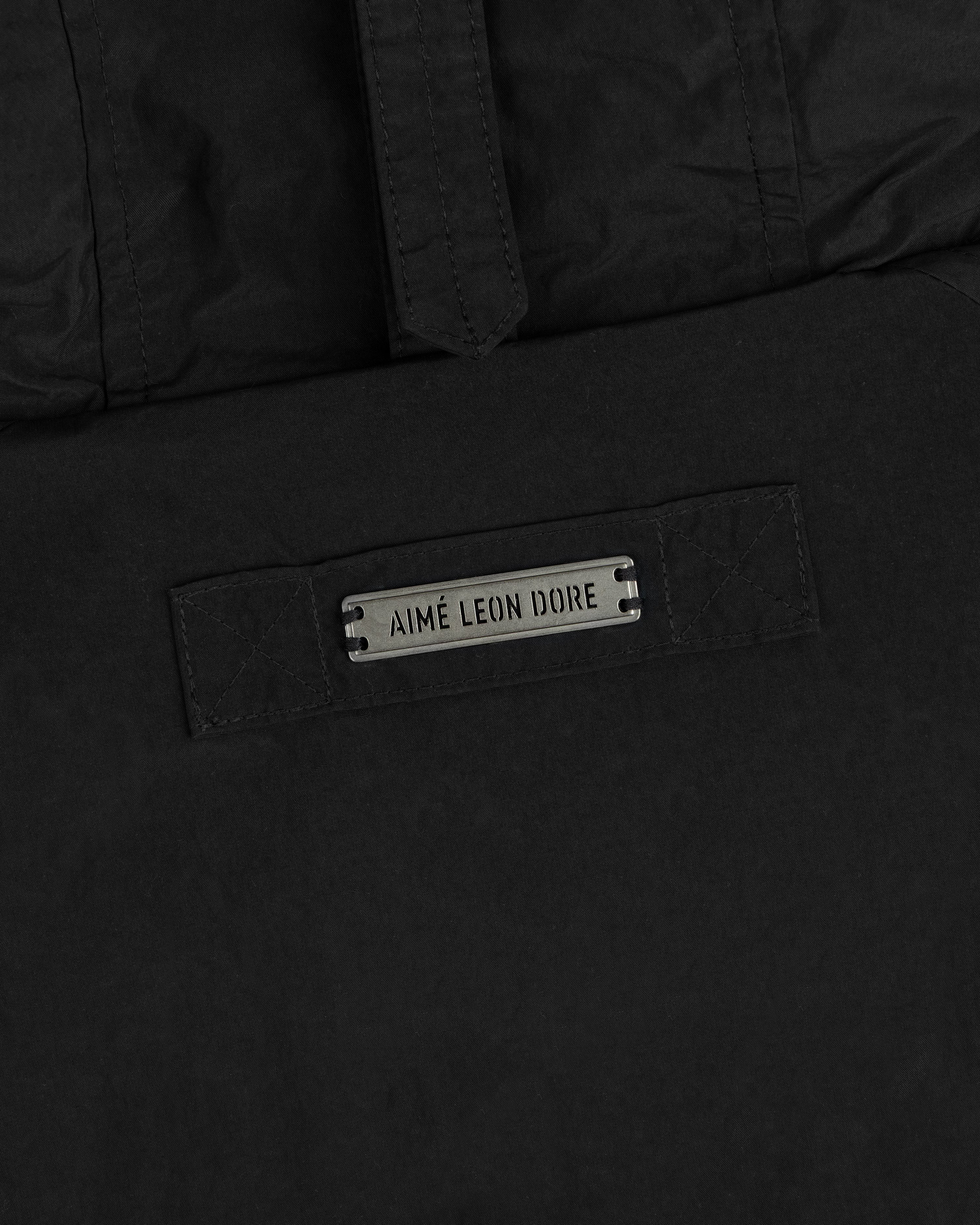 Close-up of a black Down-Filled Surplus Parka featuring a metal nameplate that reads Aimé Leon Dore.