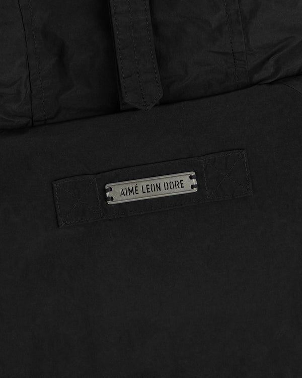 Close-up of a black Down-Filled Surplus Parka featuring a metal nameplate that reads Aimé Leon Dore.