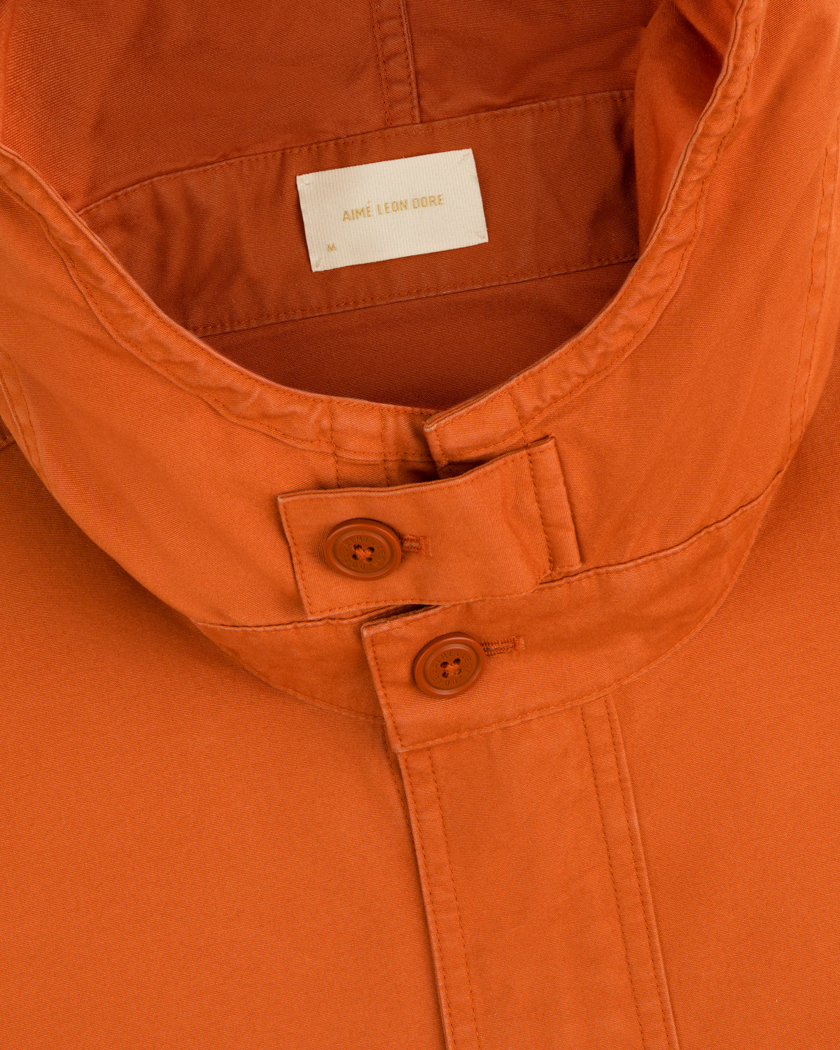 Close-up of a Garment Washed Anorak collar in orange, featuring two buttons and a branded neck label.