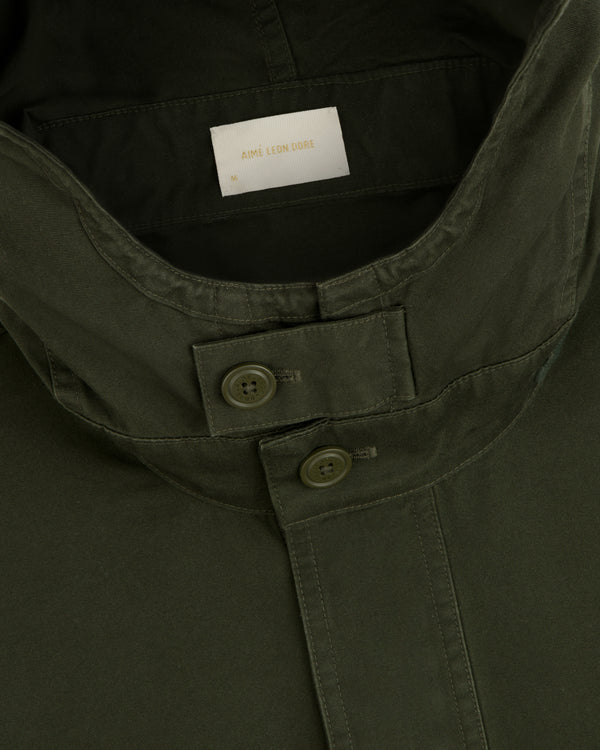 Garment Washed Anorak in olive green, featuring a buttoned throat latch and a size medium tag.