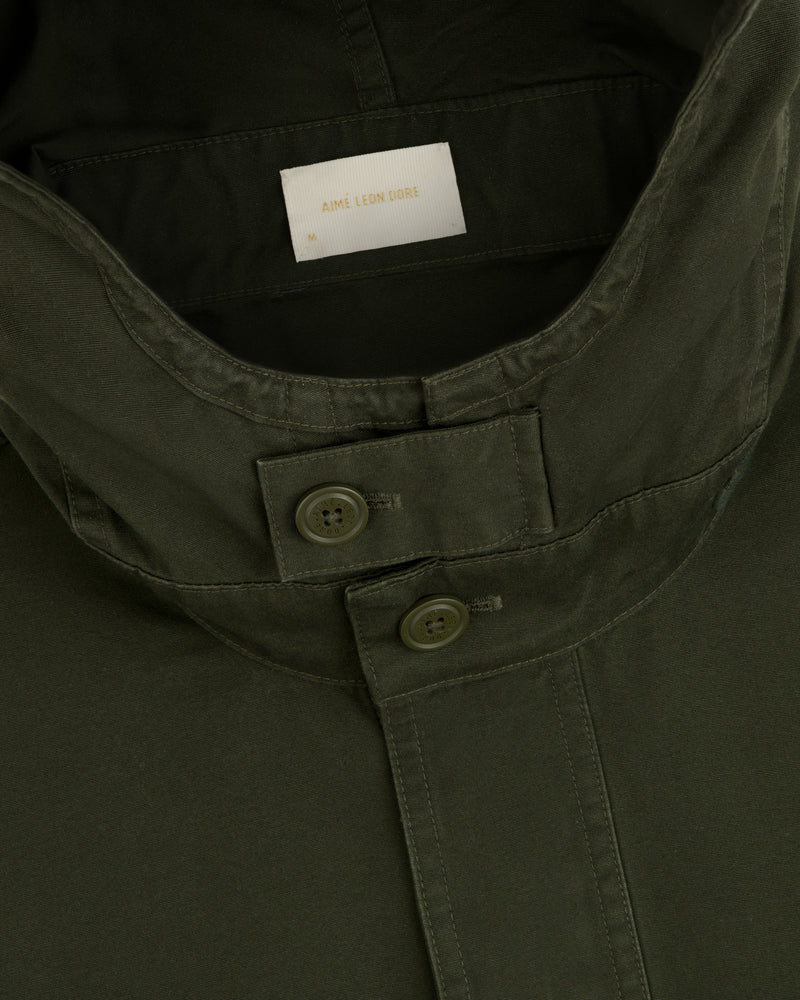Garment Washed Anorak in olive green, featuring a buttoned throat latch and a size medium tag.