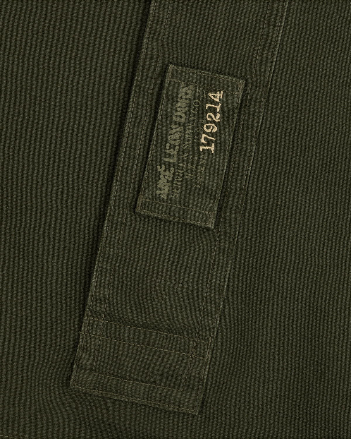 Olive green Garment Washed Anorak fabric with a rectangular patch featuring branded text and the number 179214.