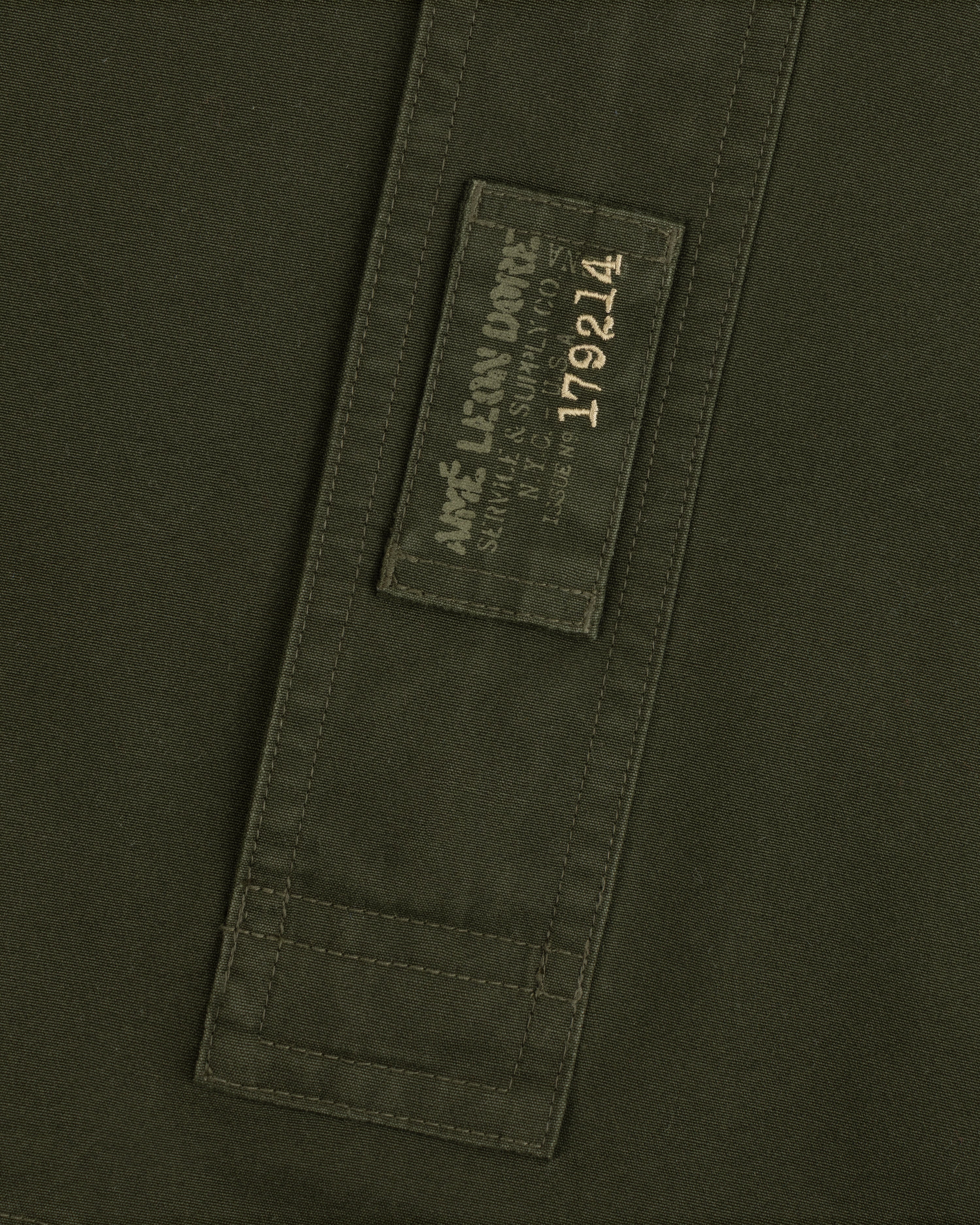 Olive green Garment Washed Anorak fabric with a rectangular patch featuring branded text and the number 179214.