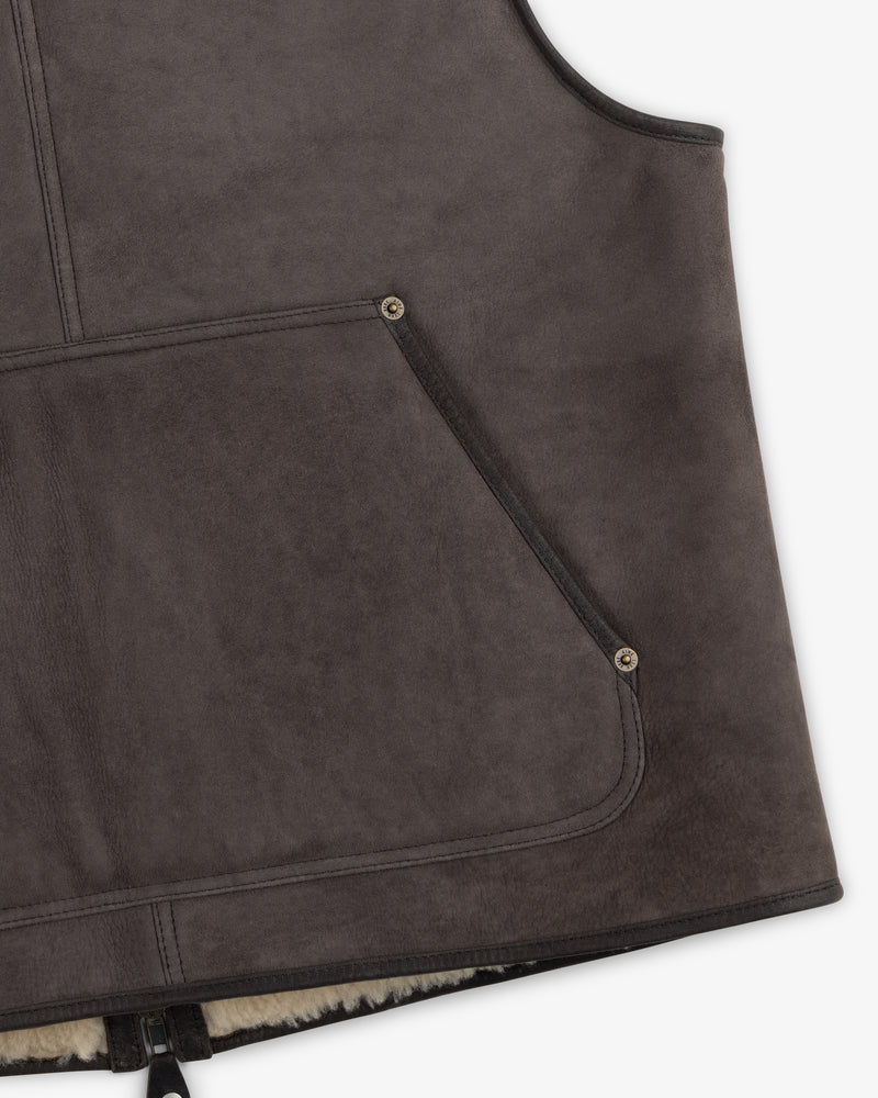 Close-up of a charcoal grey Shearling Biker Vest with a front pocket featuring metallic rivets and a shearling-lined hem.