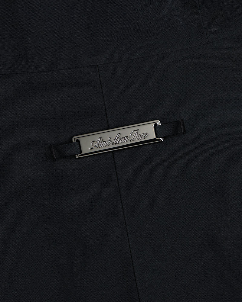 A rectangular metal Aimé Leon Dore plaque on the black fabric of a GORE-TEX Down Filled Fishtail Parka.