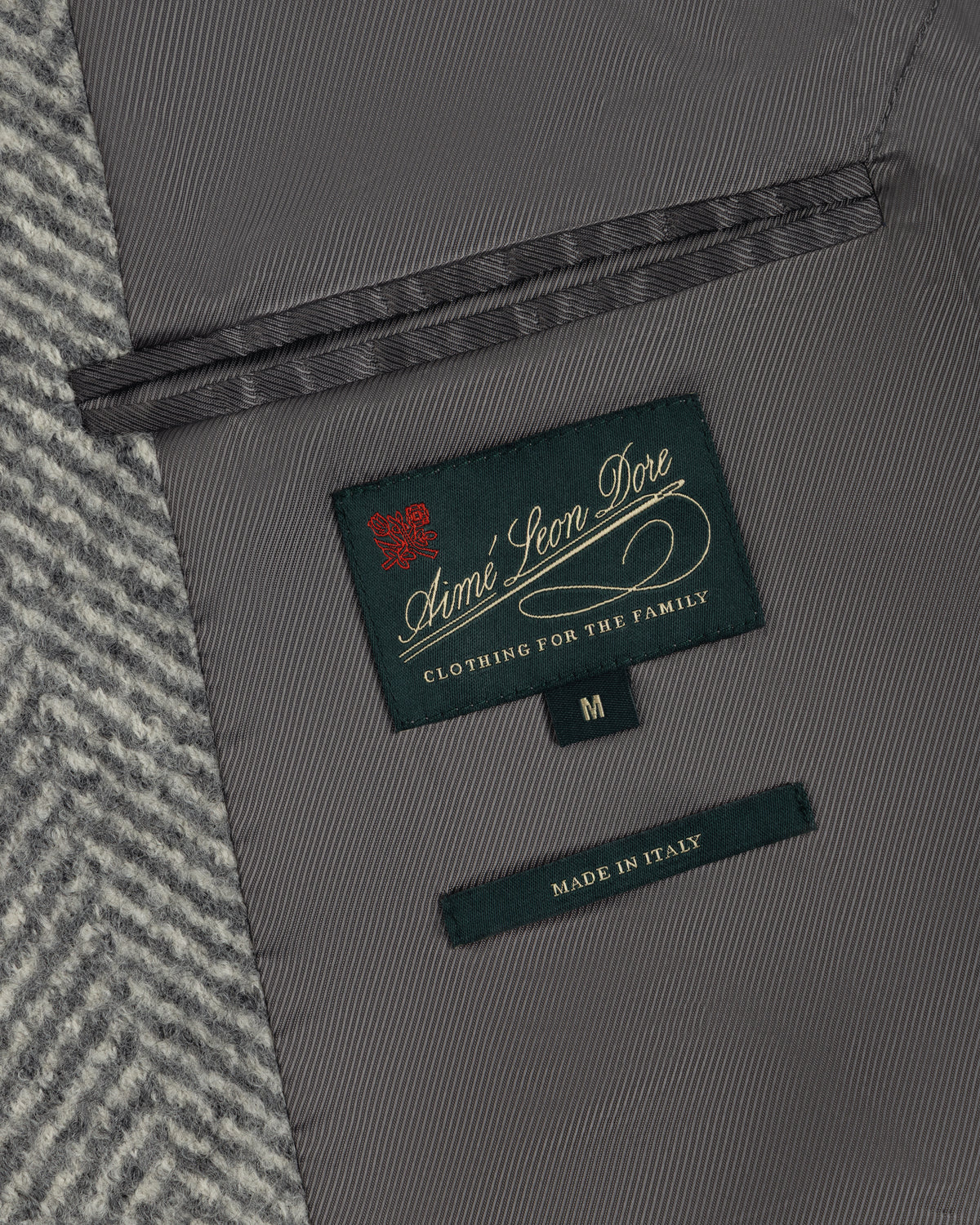 Interior of a Wool Herringbone Overcoat showing a dark green brand label, a size M tag, and a Made in Italy label.