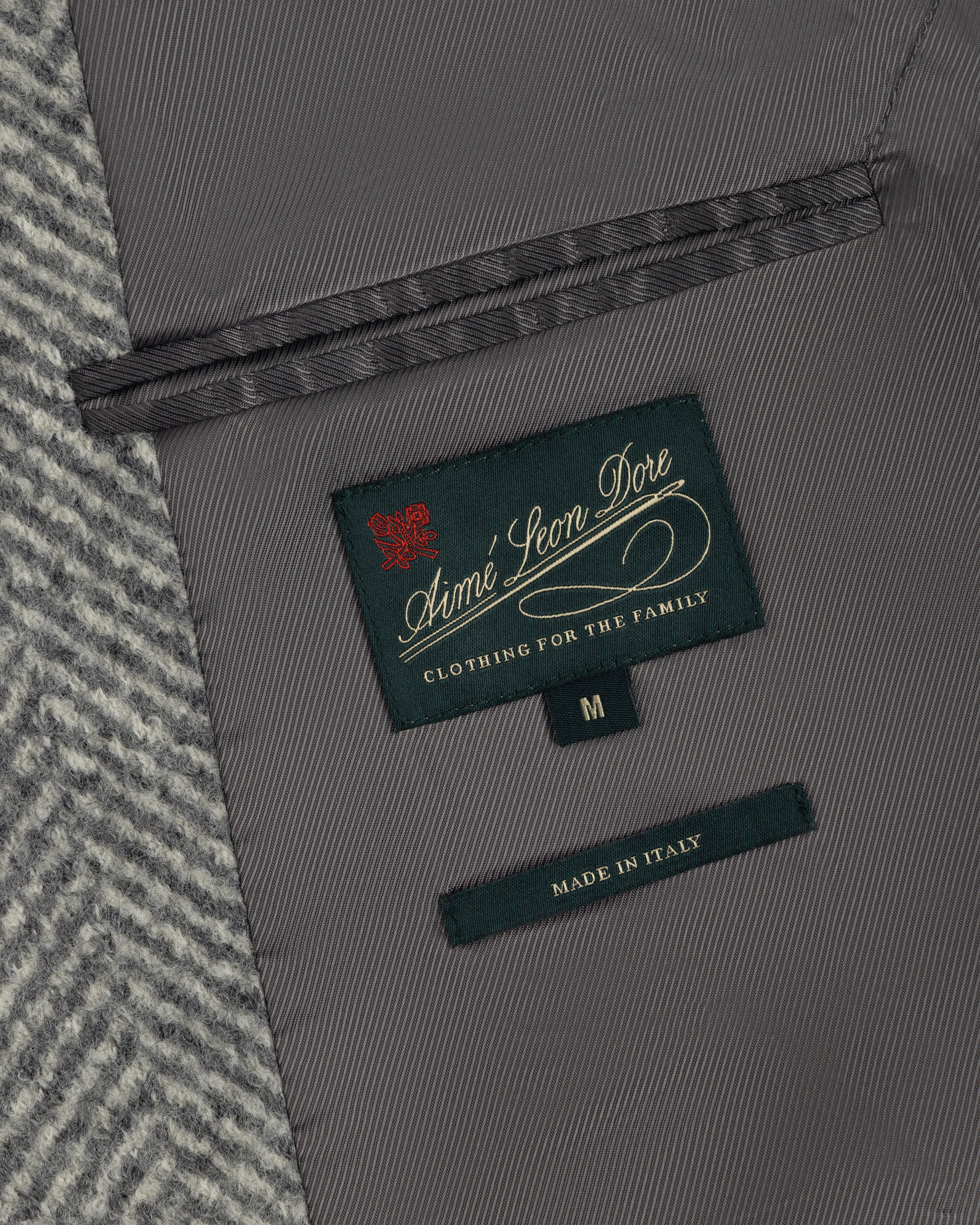 Interior of a Wool Herringbone Overcoat showing a dark green brand label, a size M tag, and a Made in Italy label.