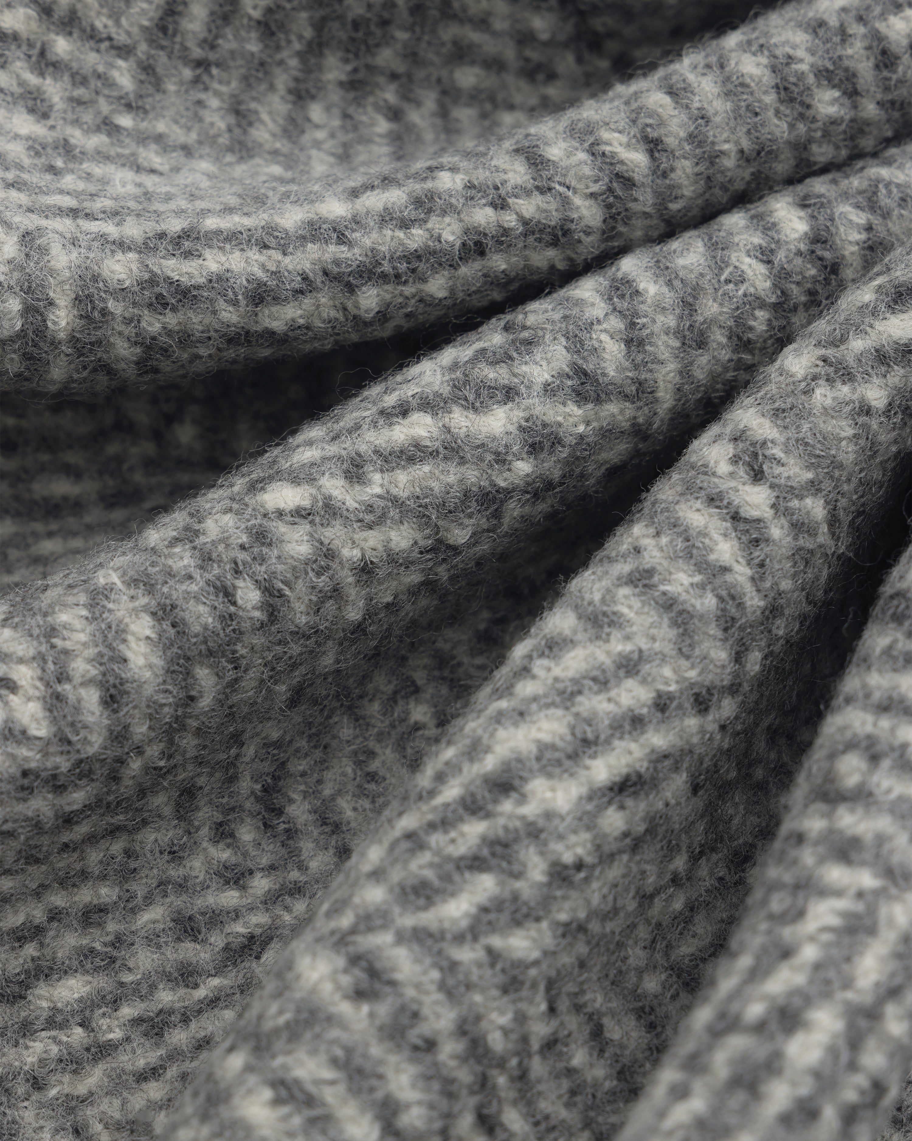Close-up of the grey and white herringbone wool fabric of a Wool Herringbone Overcoat.