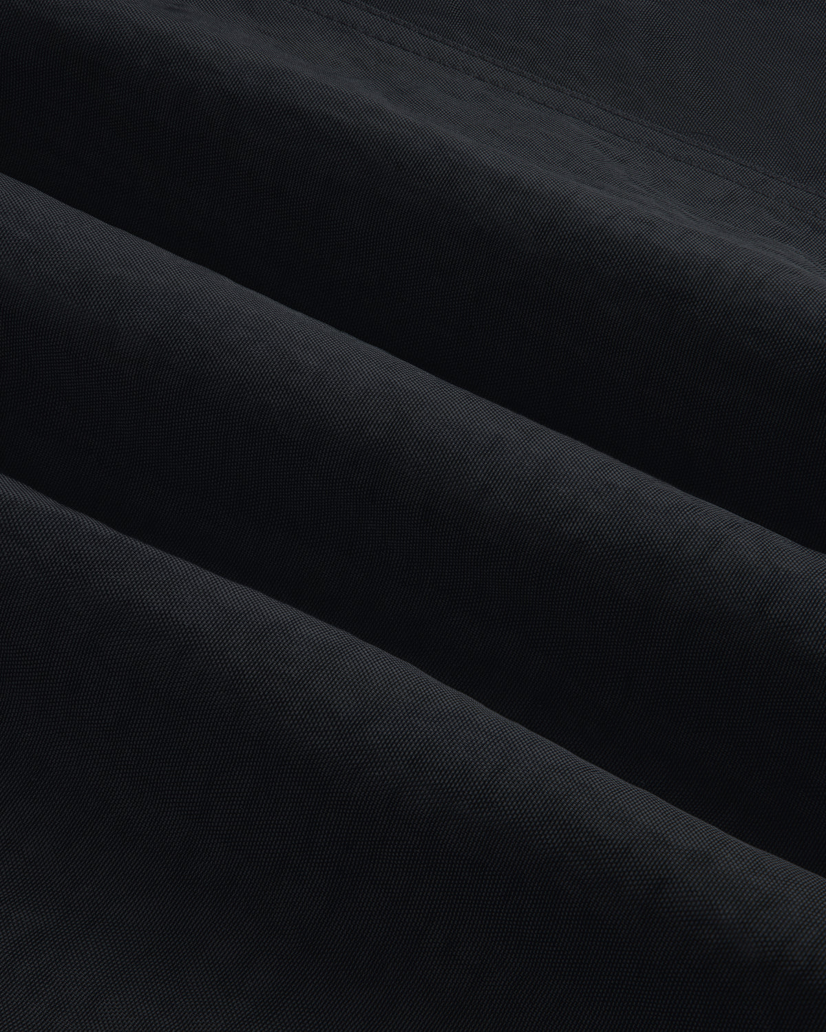 Close-up of Double Breasted Nylon Trench Coat shows soft, folded fabric with subtle horizontal ridges and shadowed texture.