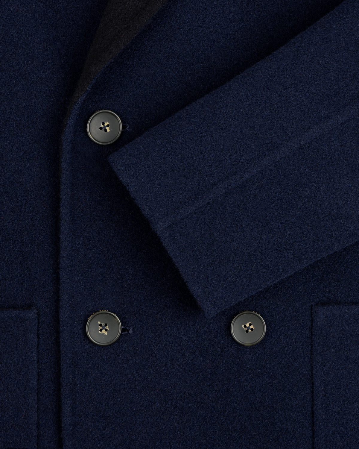 Close-up of a navy blue Reversible Double Breasted Top Coat with dark buttons and a folded sleeve.