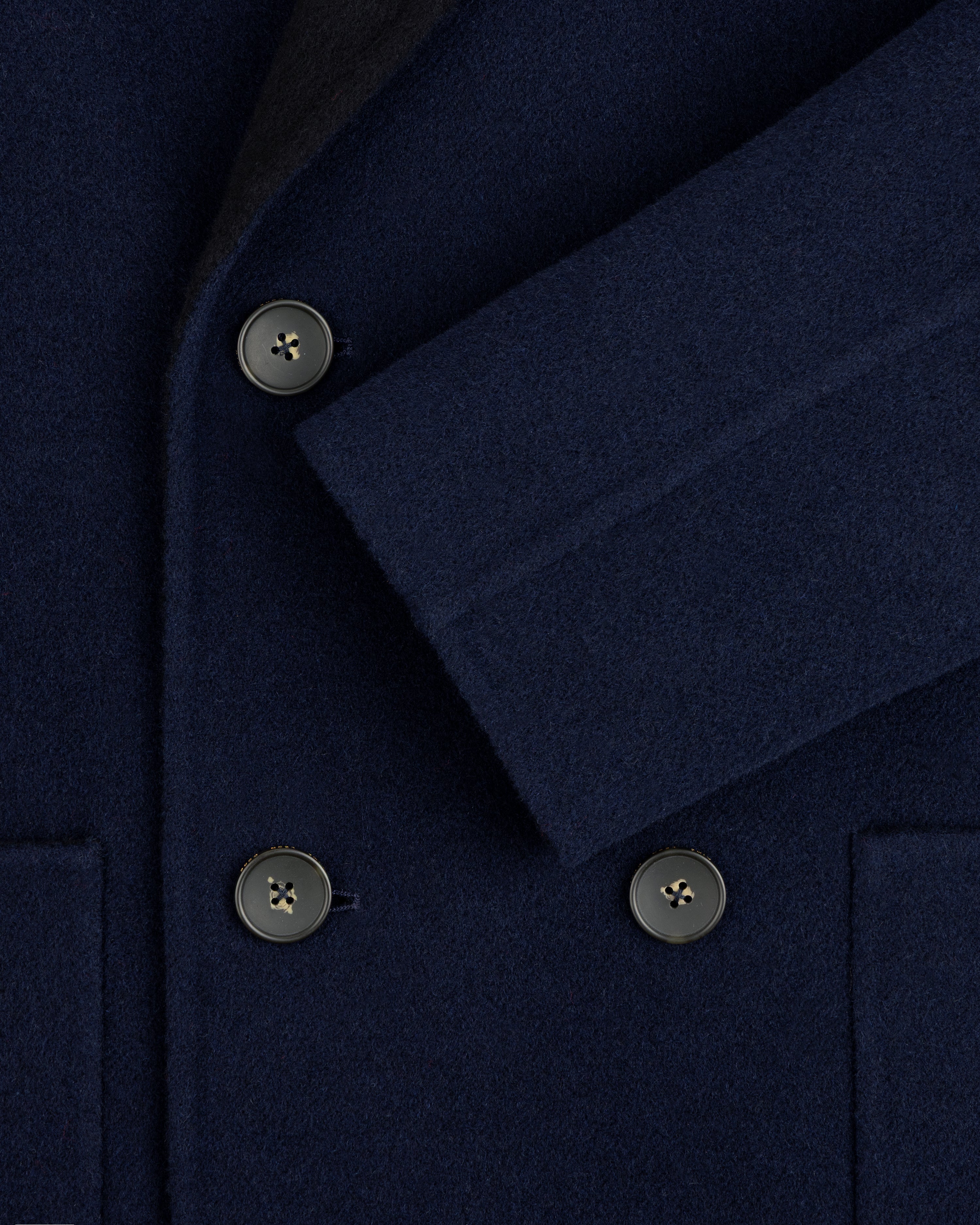 Close-up of a navy blue Reversible Double Breasted Top Coat with dark buttons and a folded sleeve.