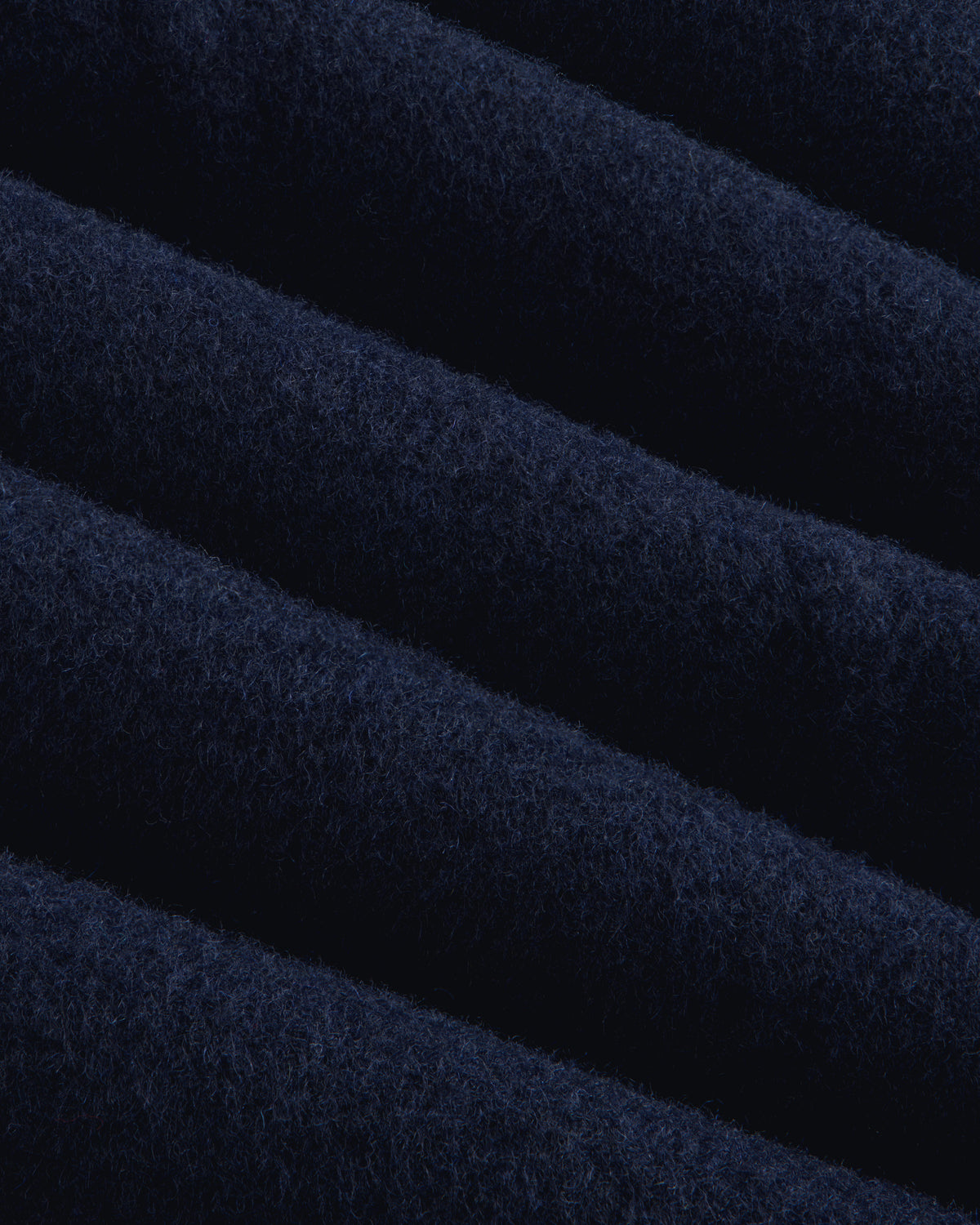 Close-up of navy blue wool fabric on a Reversible Double Breasted Top Coat with diagonal folds.
