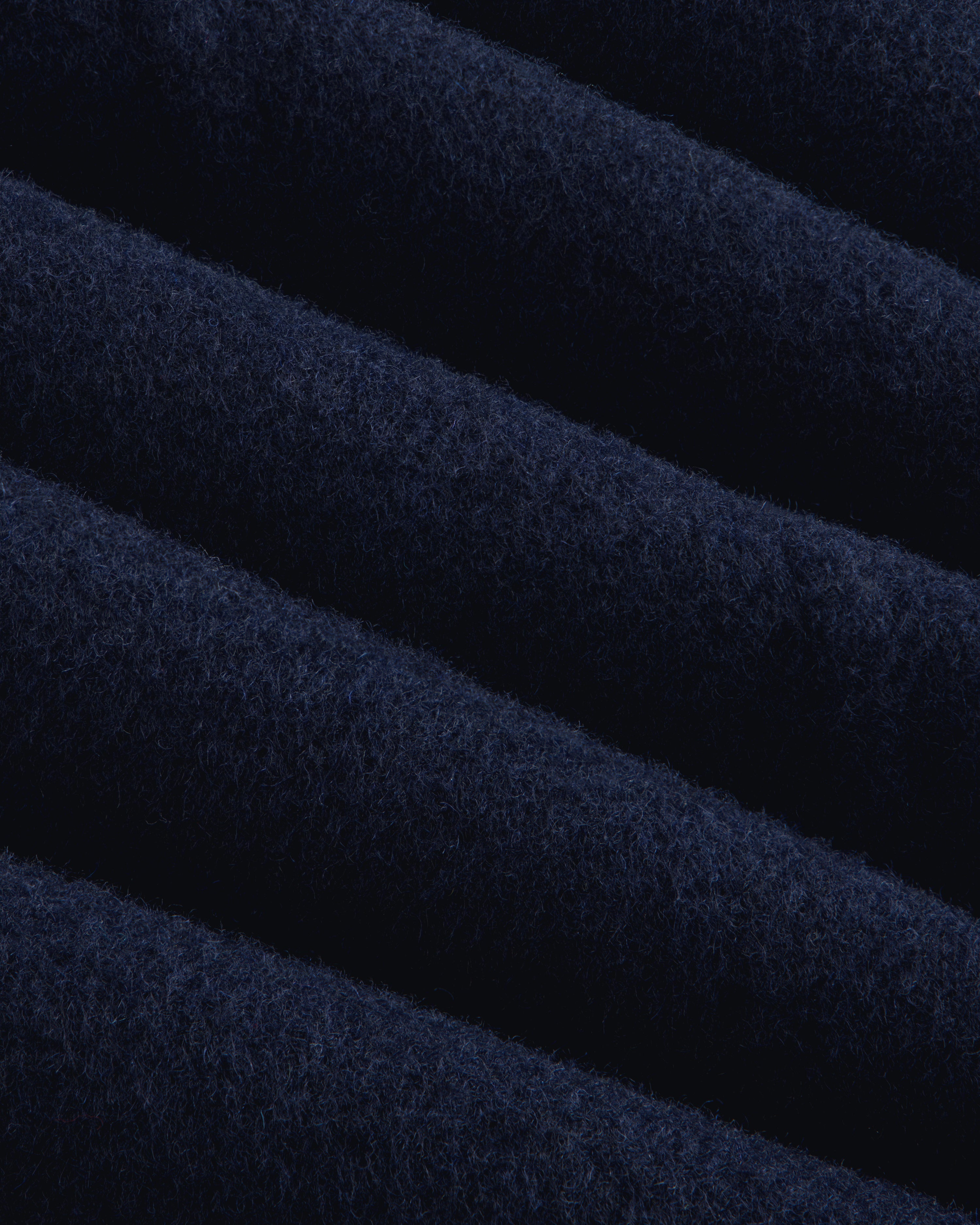 Close-up of navy blue wool fabric on a Reversible Double Breasted Top Coat with diagonal folds.
