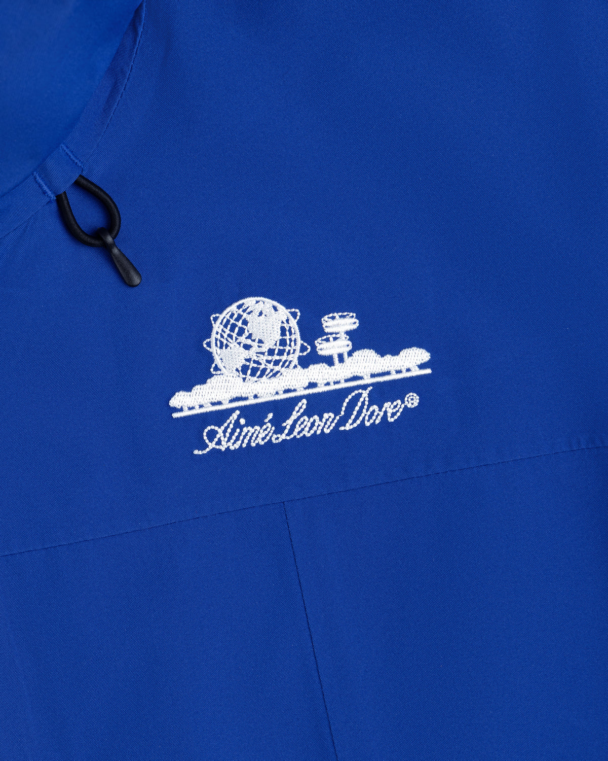 Close-up of a royal blue Cropped GORE-TEX Shell Jacket featuring an embroidered white globe logo and Aimé Leon Dore text.
