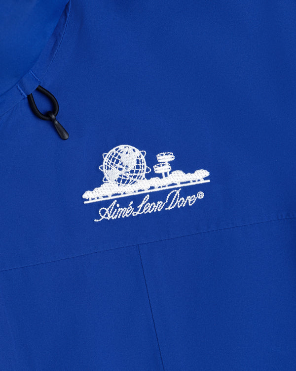 Close-up of a royal blue Cropped GORE-TEX Shell Jacket featuring an embroidered white globe logo and Aimé Leon Dore text.