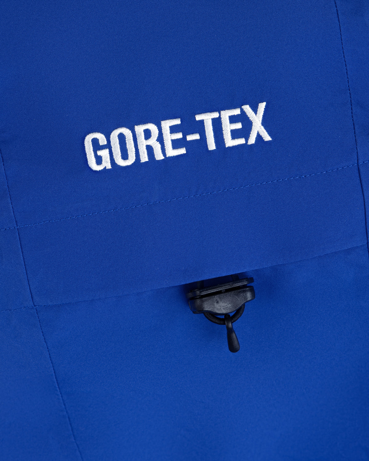 Close-up of a blue Cropped GORE-TEX Shell Jacket with embroidered white text and a small black toggle cord.