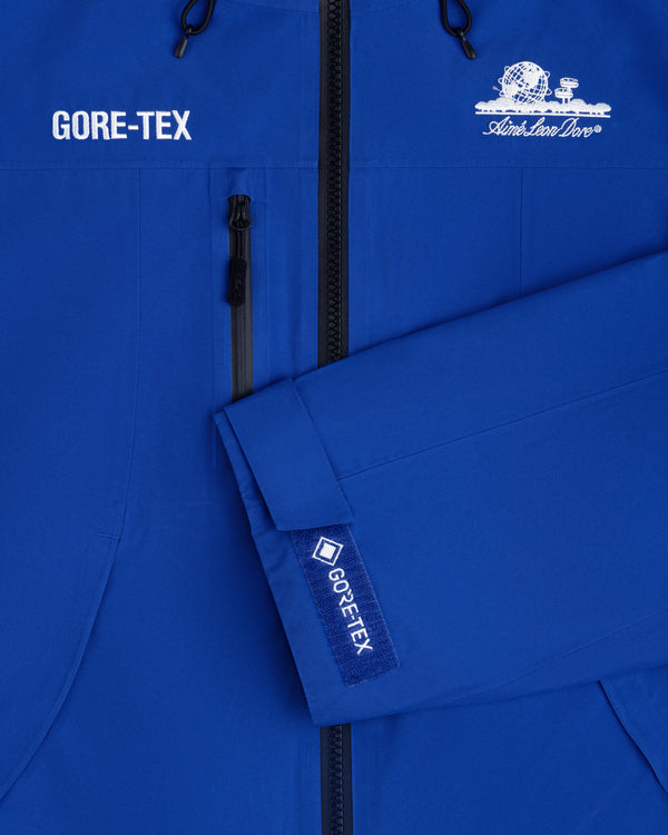 Close-up of a blue Cropped GORE-TEX Shell Jacket with a chest zipper and an embroidered globe logo.