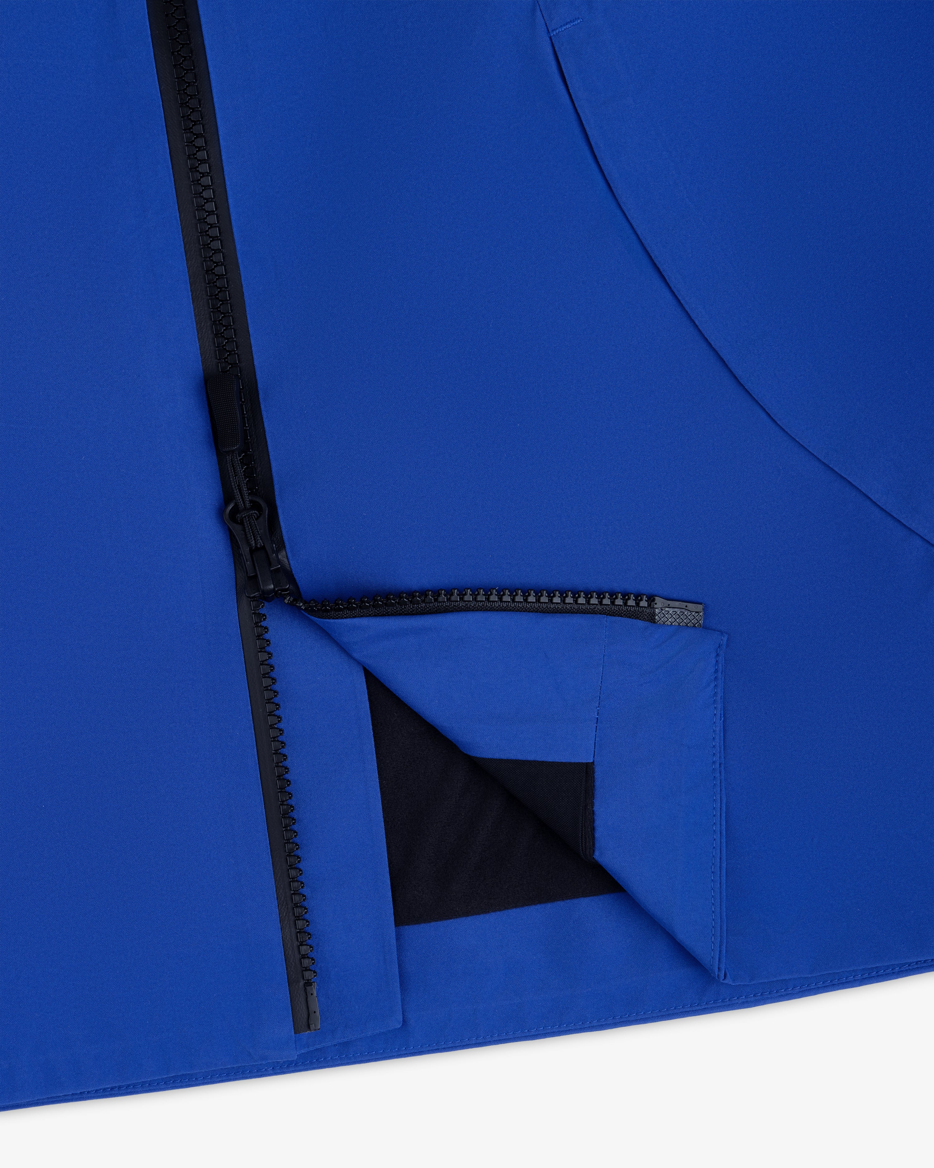 Close-up of a blue Cropped GORE-TEX Shell Jacket with a black front zipper and a partially open hem.