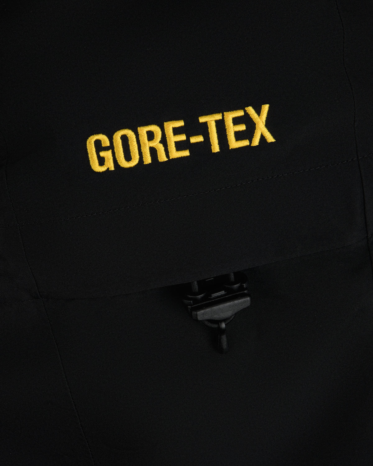 Close-up of yellow GORE-TEX embroidery on a black Cropped GORE-TEX Shell Jacket with a drawstring toggle.
