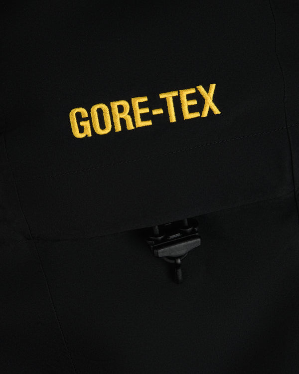 Close-up of yellow GORE-TEX embroidery on a black Cropped GORE-TEX Shell Jacket with a drawstring toggle.