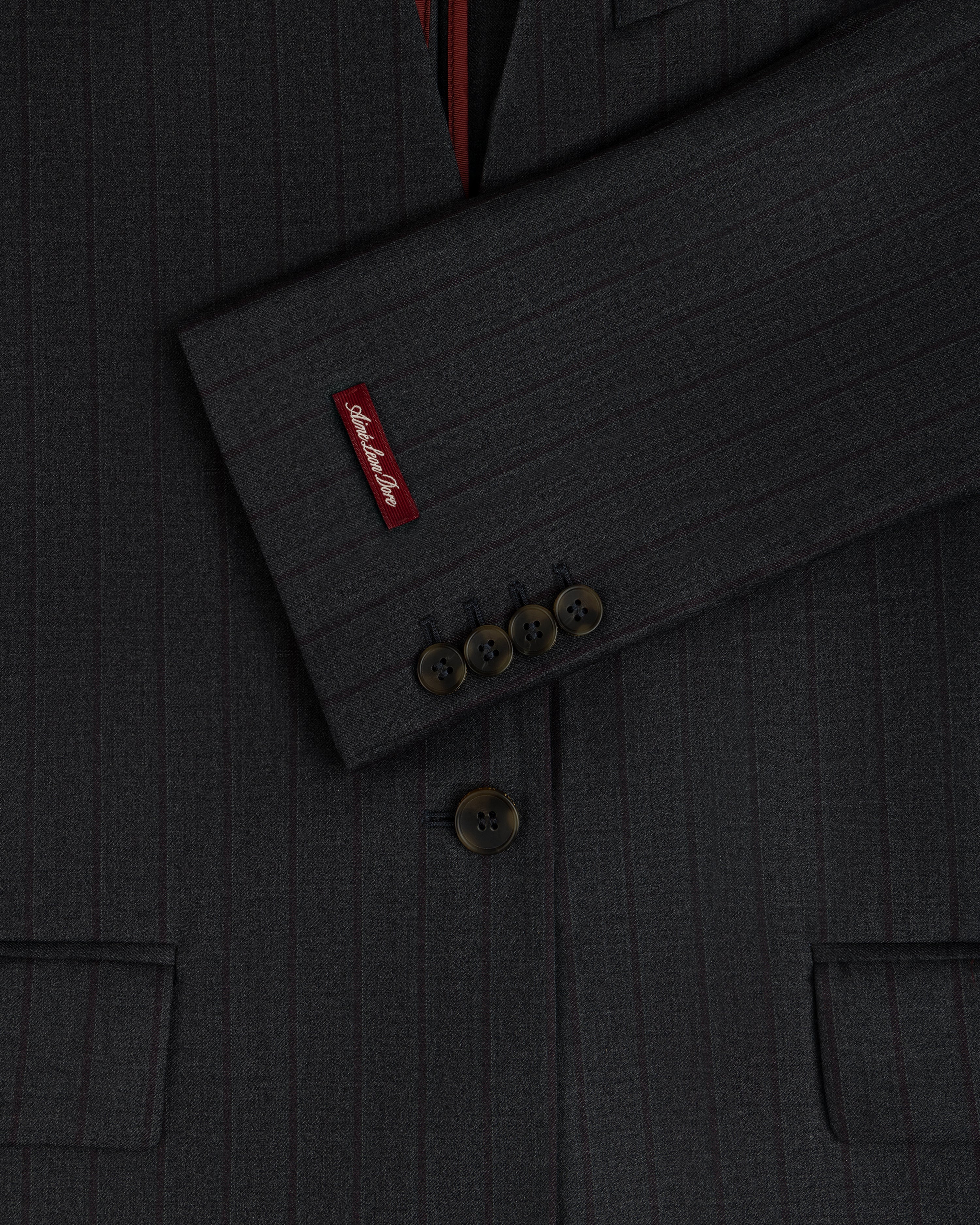 Close-up of a Collarless Striped Blazer sleeve with four charcoal pinstriped buttons and a branded red tag.