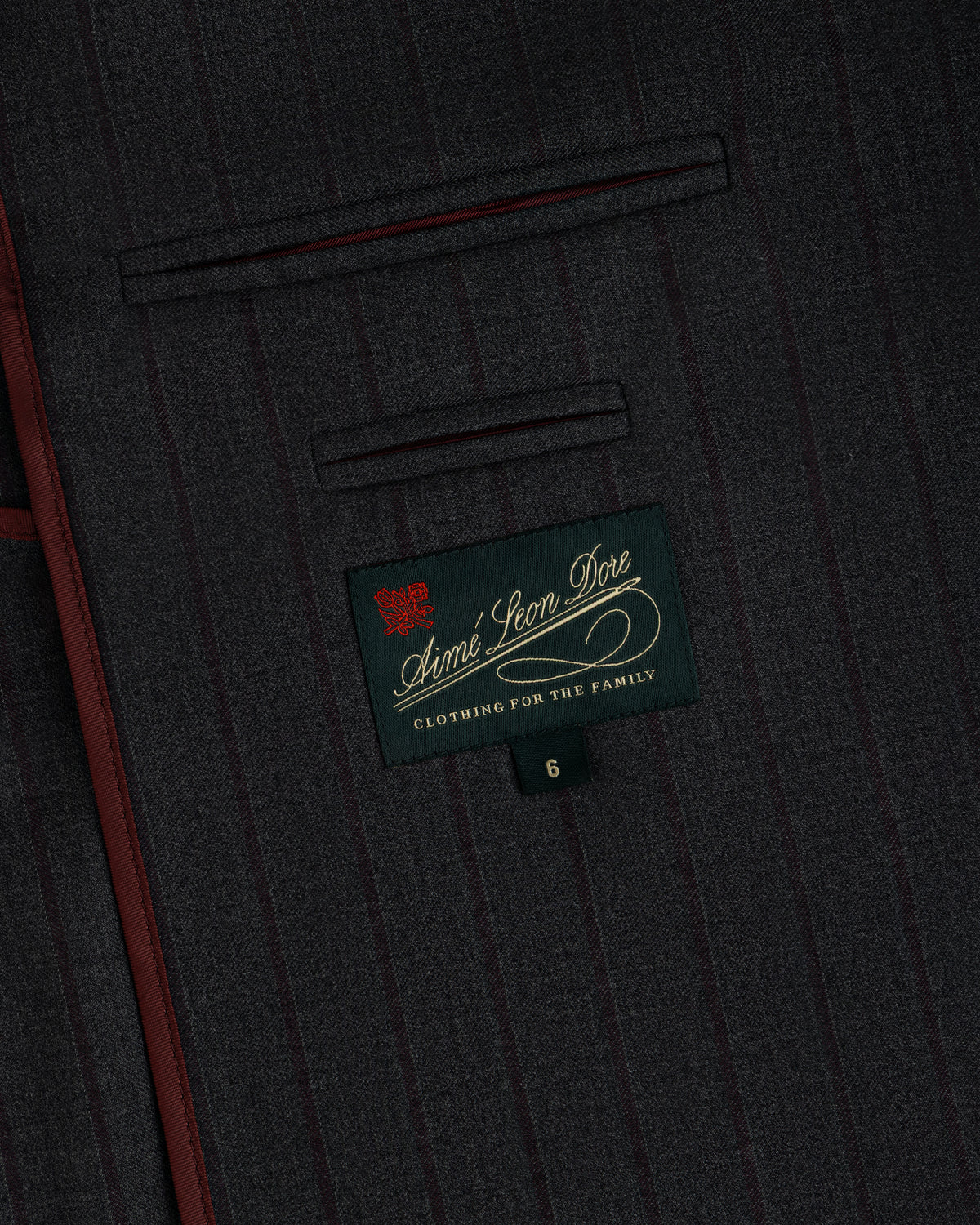 Collarless Striped Blazer in dark gray pinstriped fabric with a rectangular Aimé Leon Dore label and a size six tag.