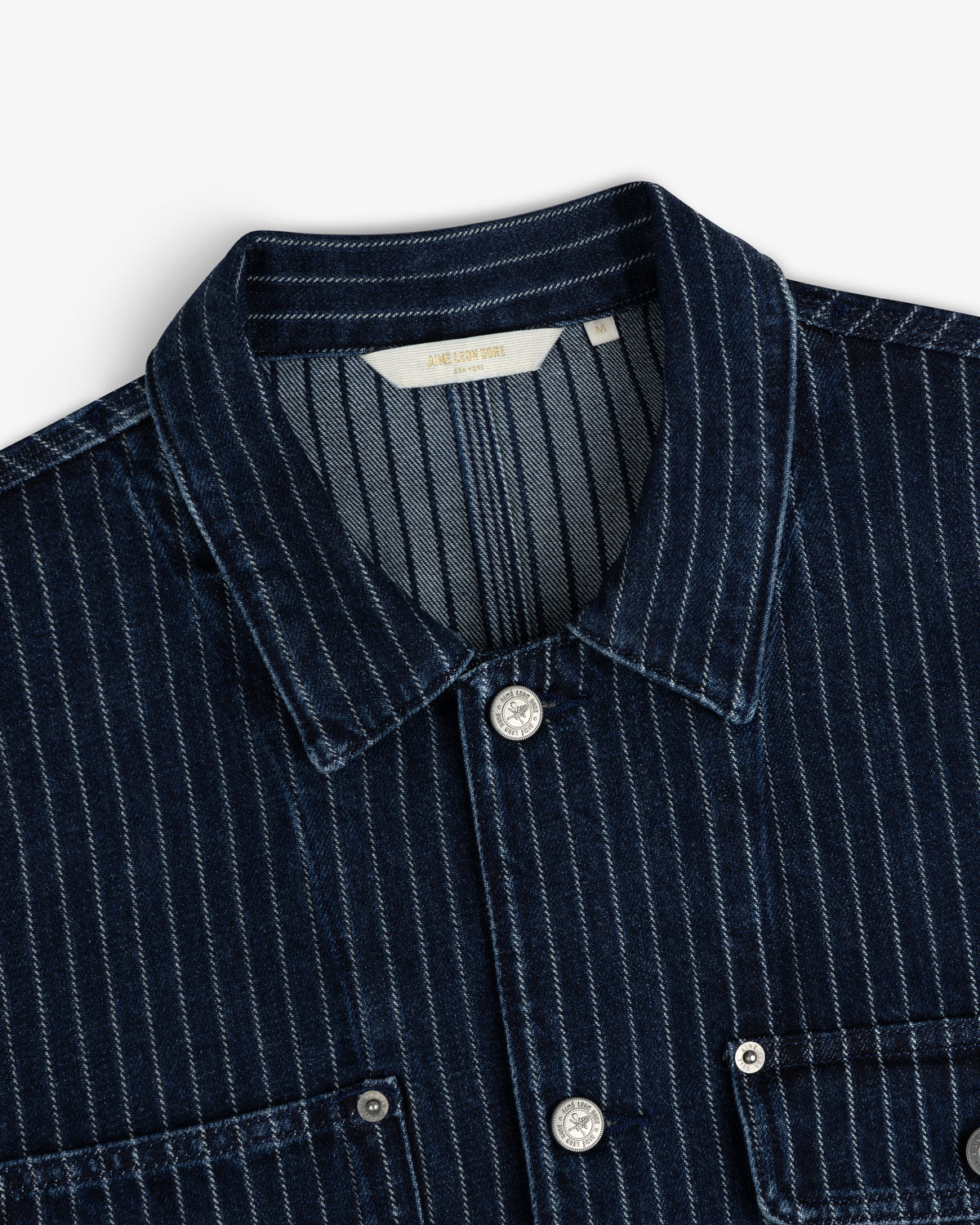 Chalk Stripe Denim Trucker Jacket in dark blue with white stripes, collar, silver buttons, and chest pockets shown close up.