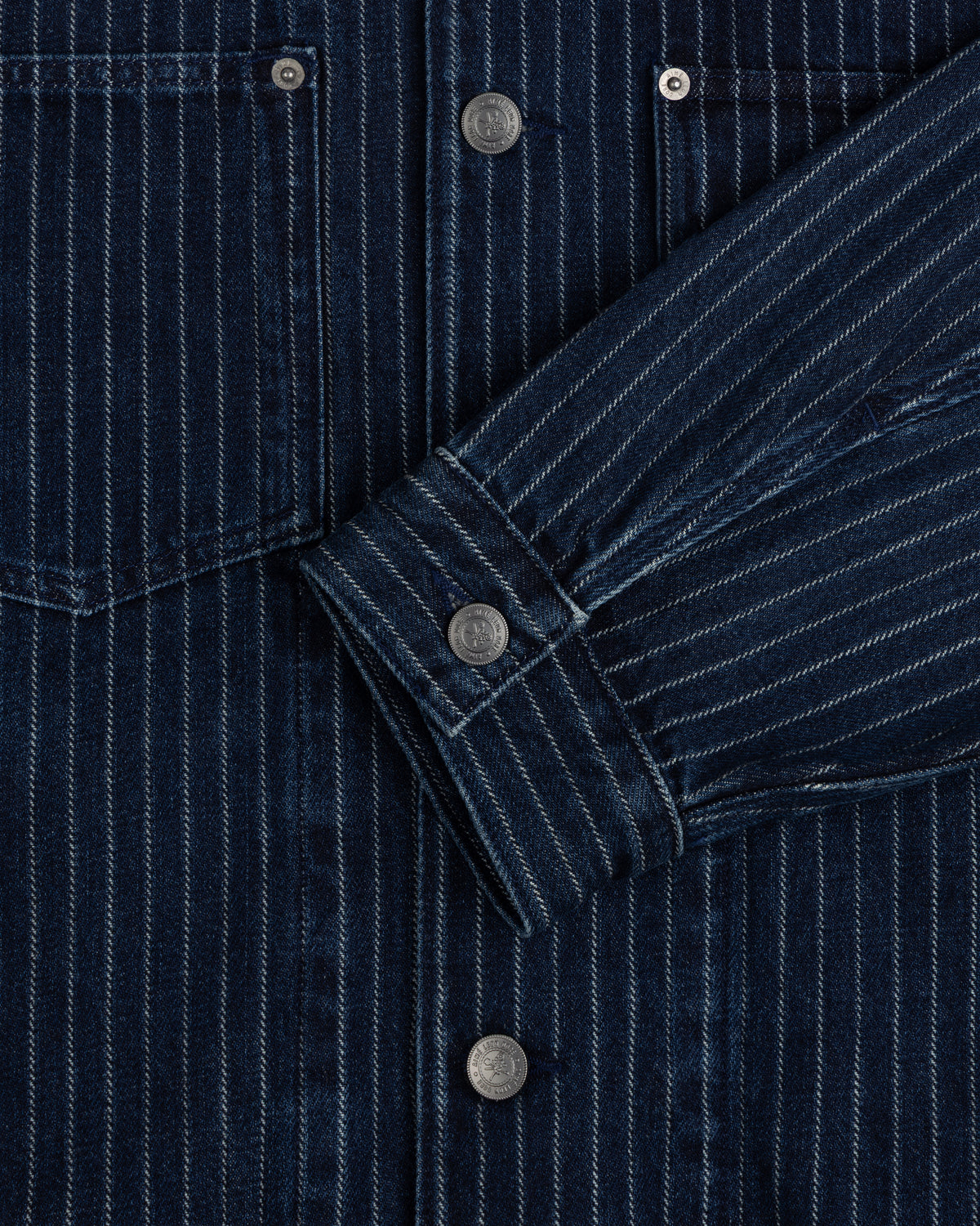 Close-up of the Chalk Stripe Denim Trucker Jacket featuring dark blue pinstripes, metal buttons, and a front pocket.